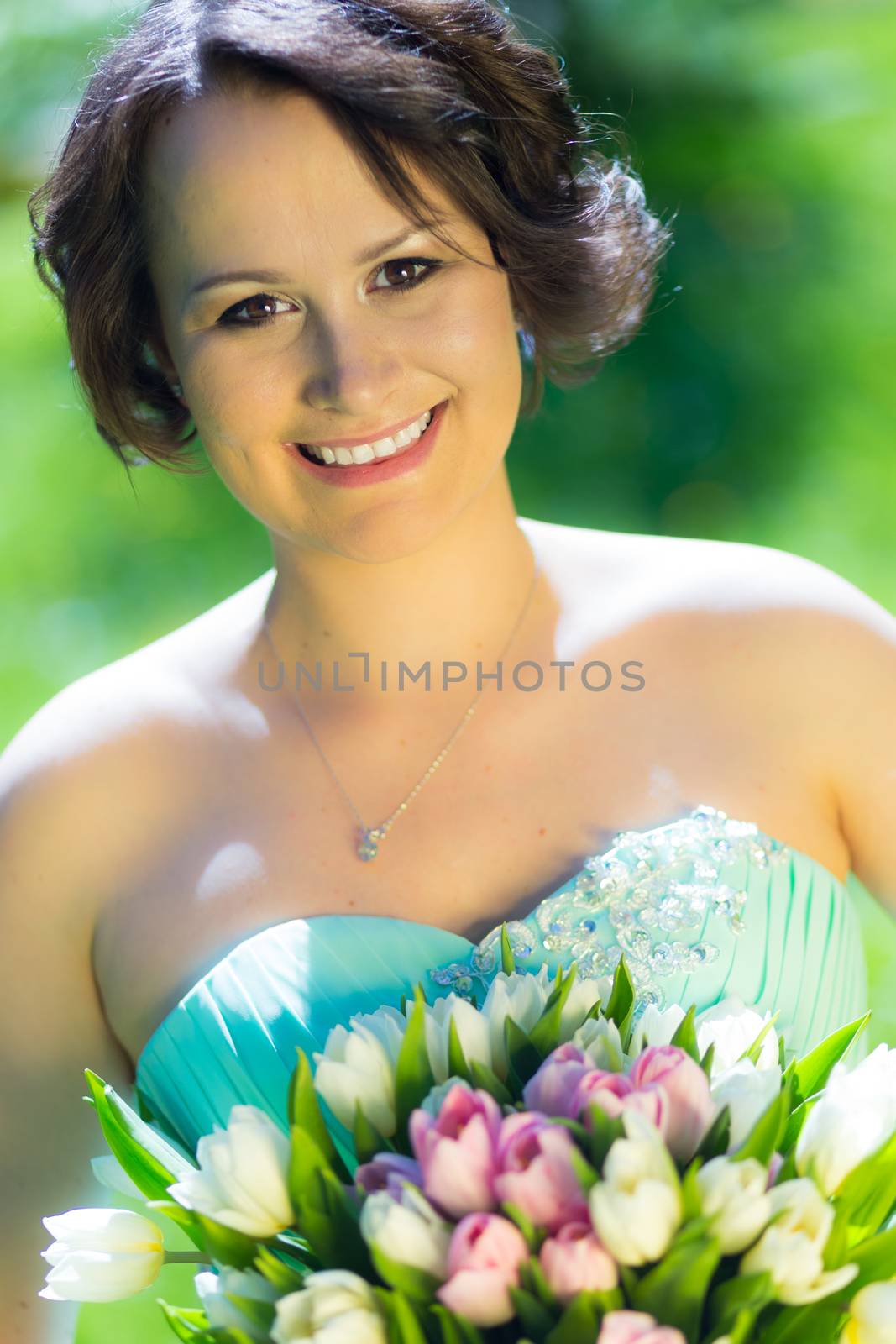 Portrait of a beautiful woman in green dress holding a colorful bouquet of tulips.