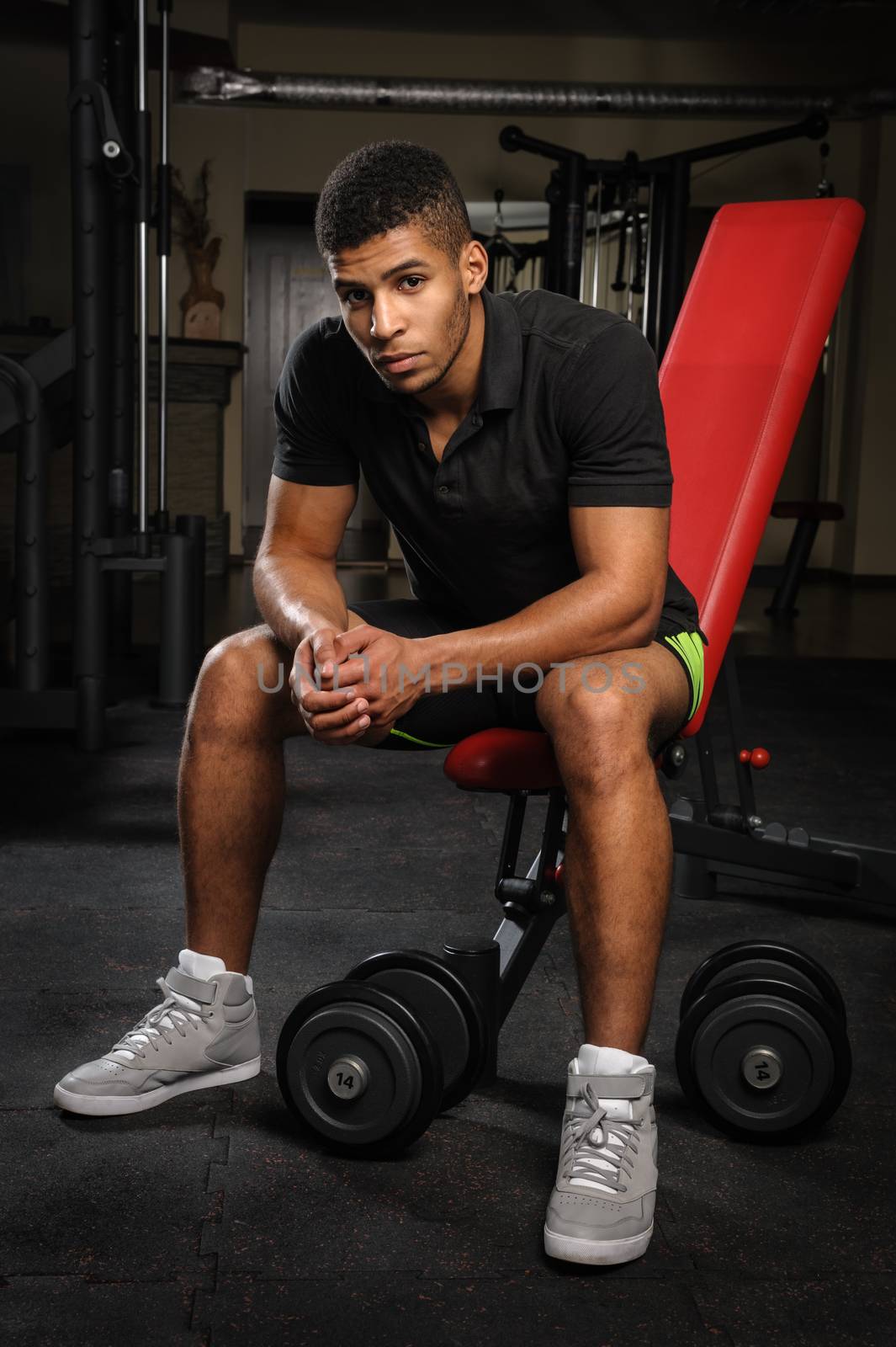 handsome young african descent mixed race man sitting and resting on bench in gym
