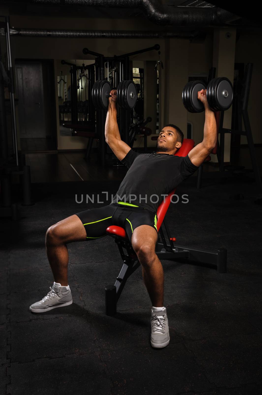handsome young african descent mixed race man doing bench dumbbell press workout in gym