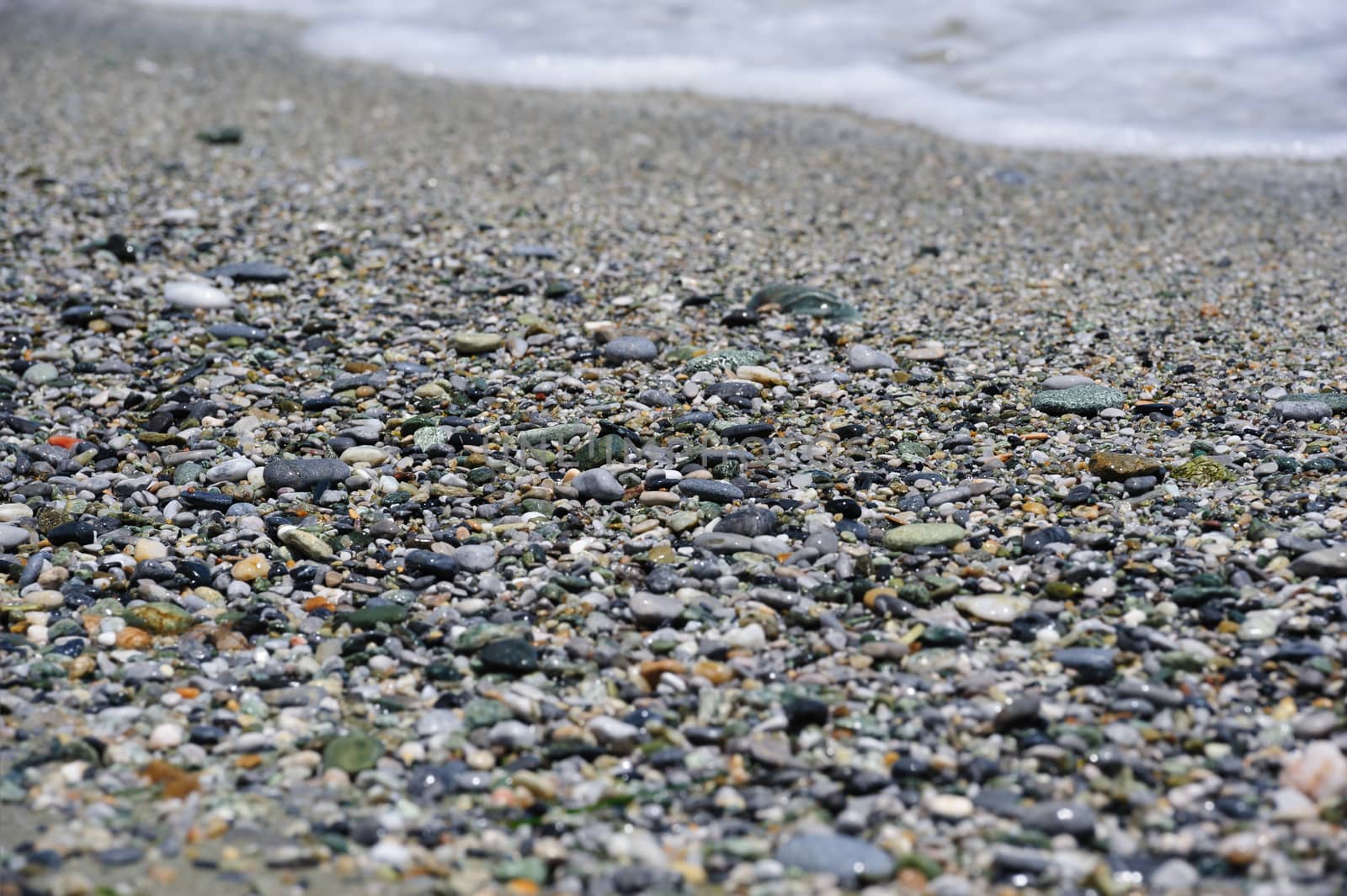 Sea multicolored pebbles, gravel beach in sunlight, selective focus, background