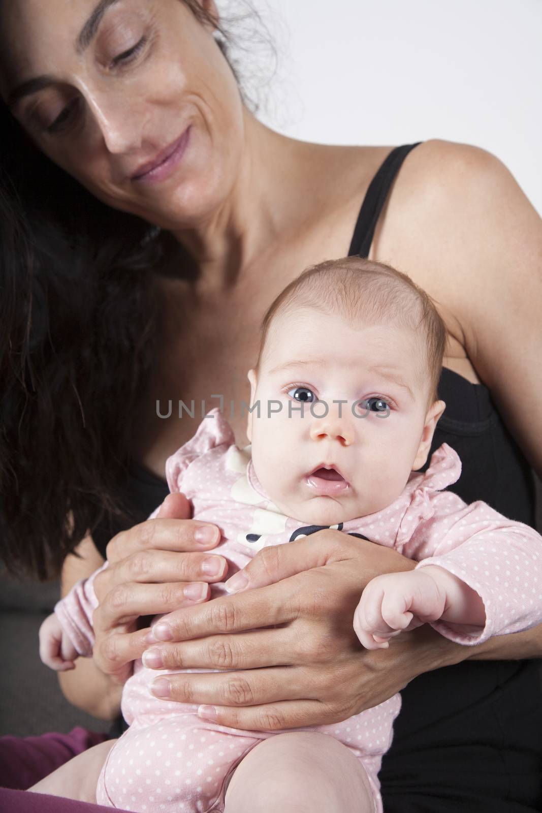 portrait of two month age baby pink onesie shirt open eyes surprise looking sitting on  brunette woman mother leg purple trousers