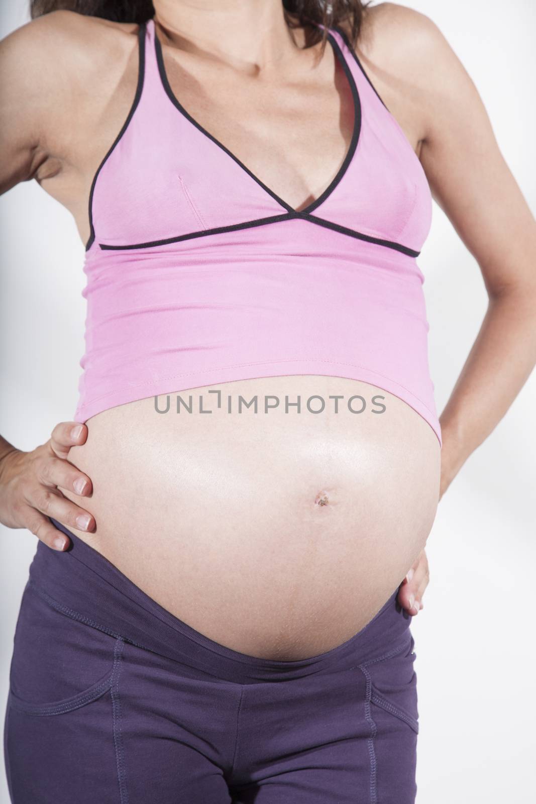 eight month brunette pregnant woman naked paunch belly button pink shirt purple trousers hands on hips standing isolated on white