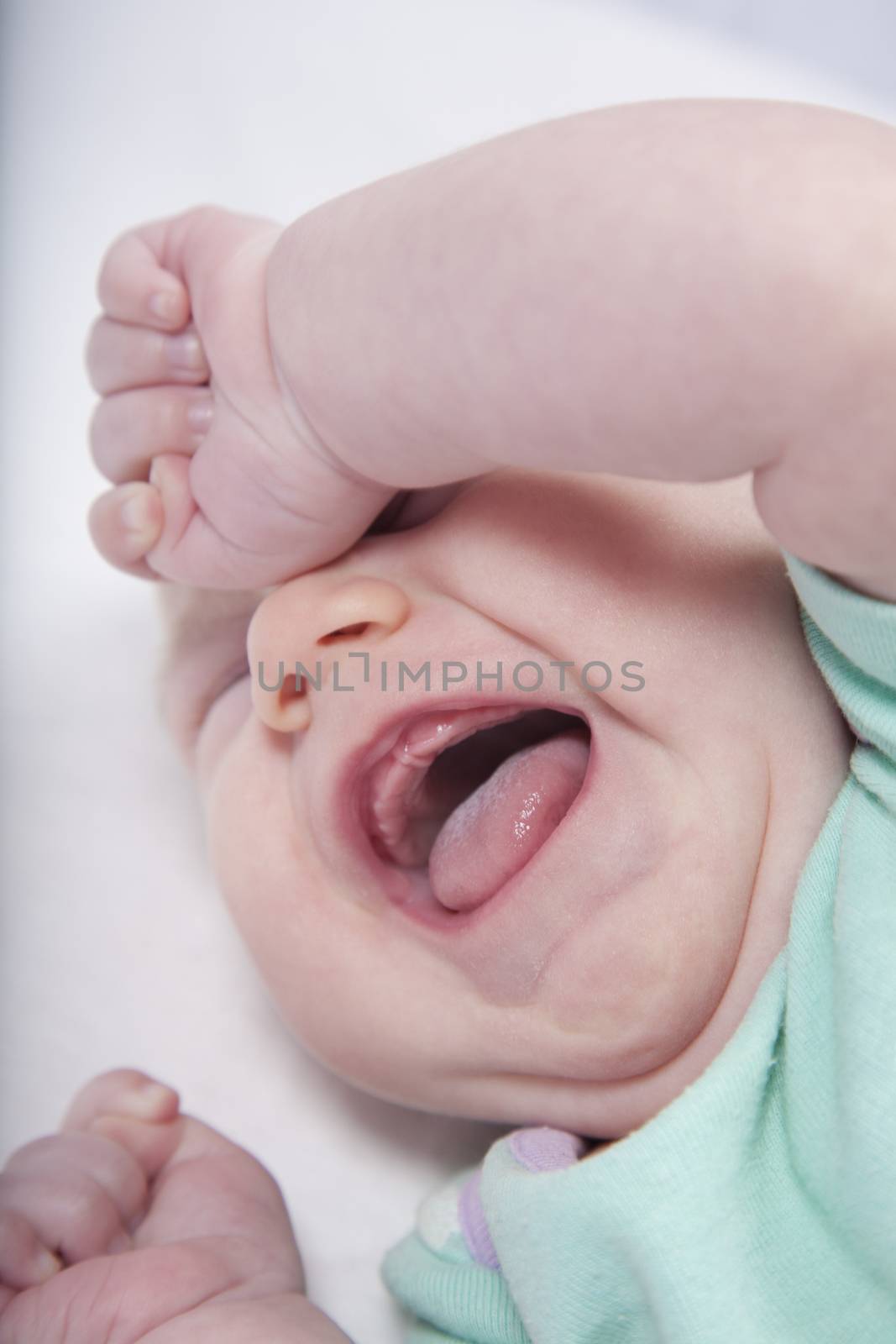 one month age baby green onesie shirt crying and shout close eyes tongue over white bedcover