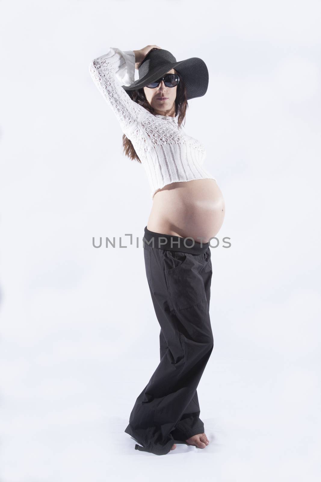 eight months brunette pregnant woman bare tummy belly button wool top sweater black sunglasses big pamela hat posing as fashion model isolated on white