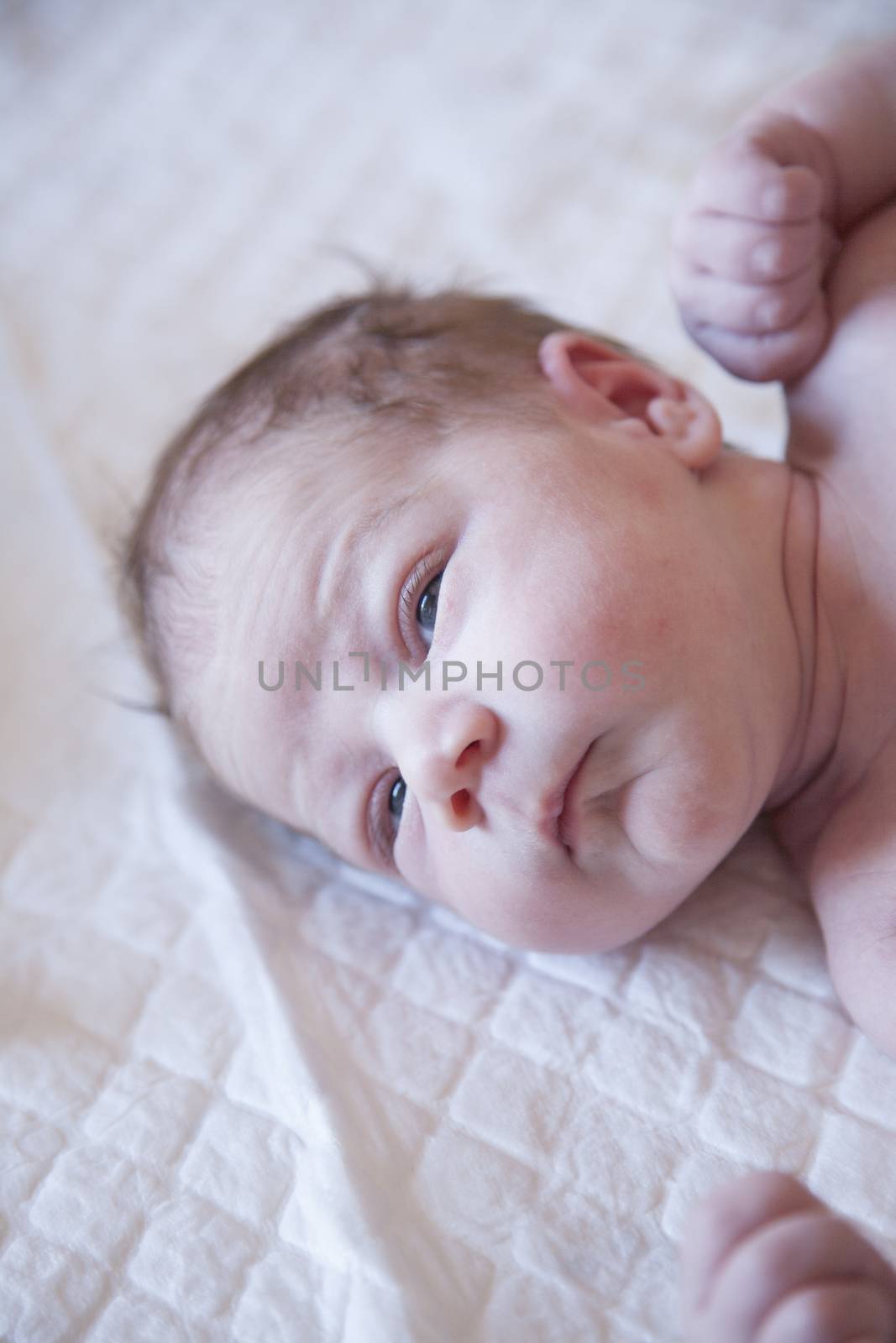 nine days age naked bare newborn baby face and irritated skin open eyes looking at camera over white bedcover