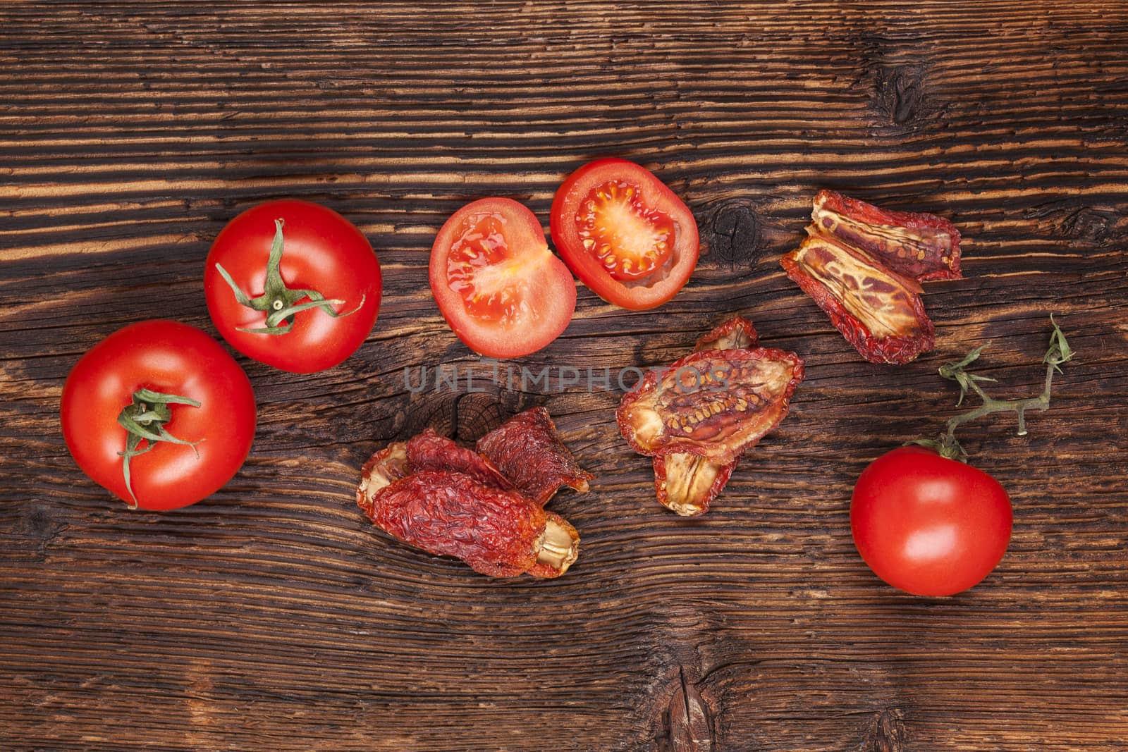 Delicious sundried and fresh tomatoes on brown wooden vintage textured background, top view. Traditional mediterranean kitchen.