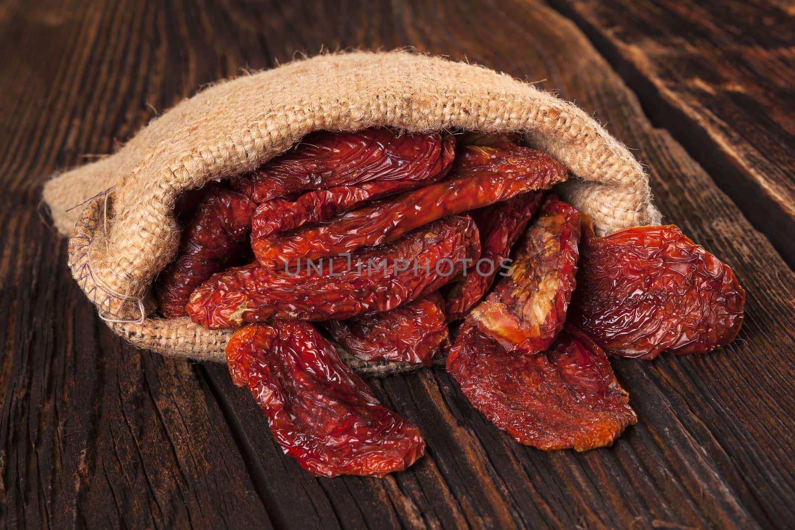 Delicious dried tomatoes in burlap bag on brown wooden vintage textured background. Traditional mediterranean kitchen.