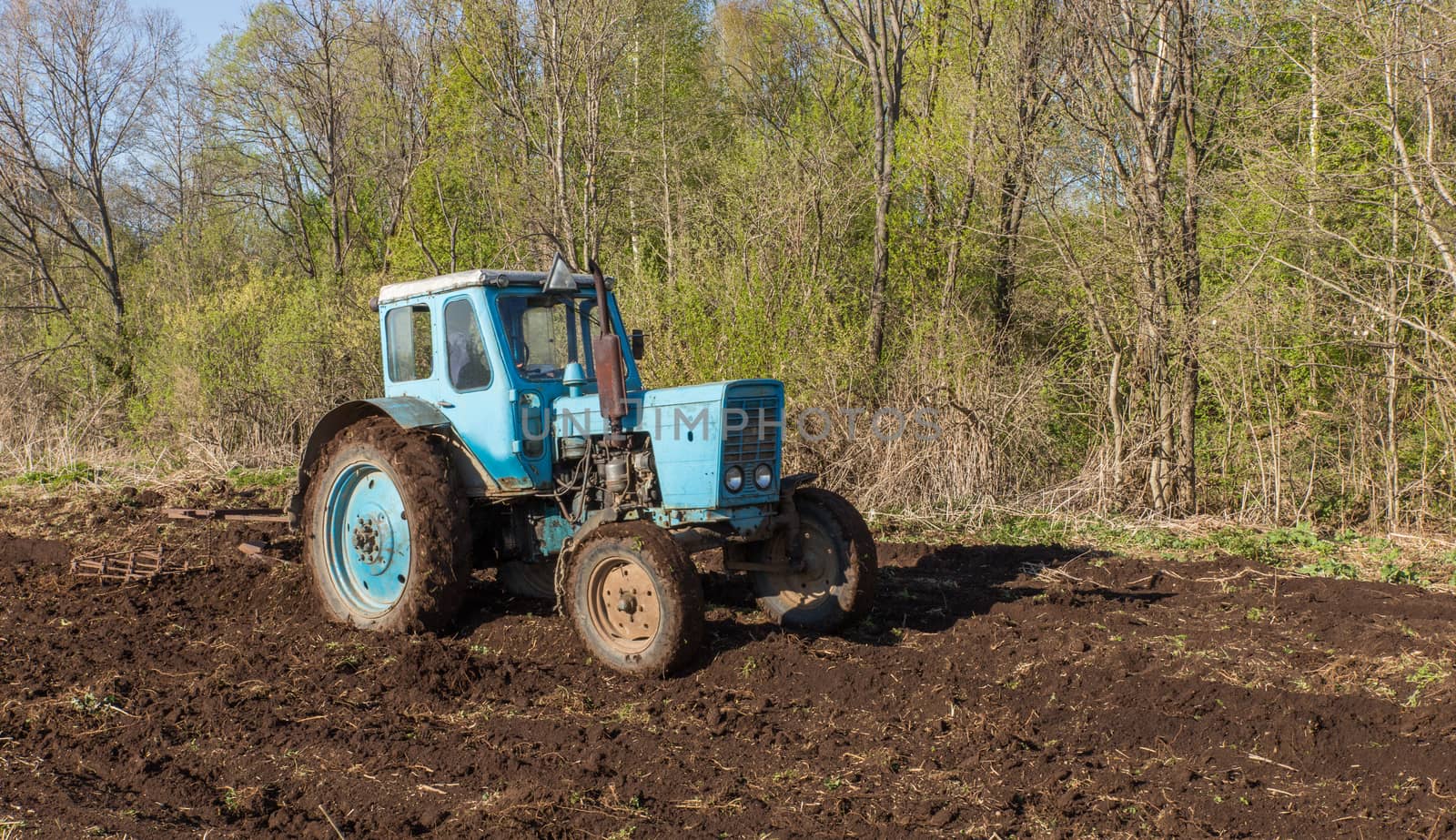 Blue tractor plowing a field in spring