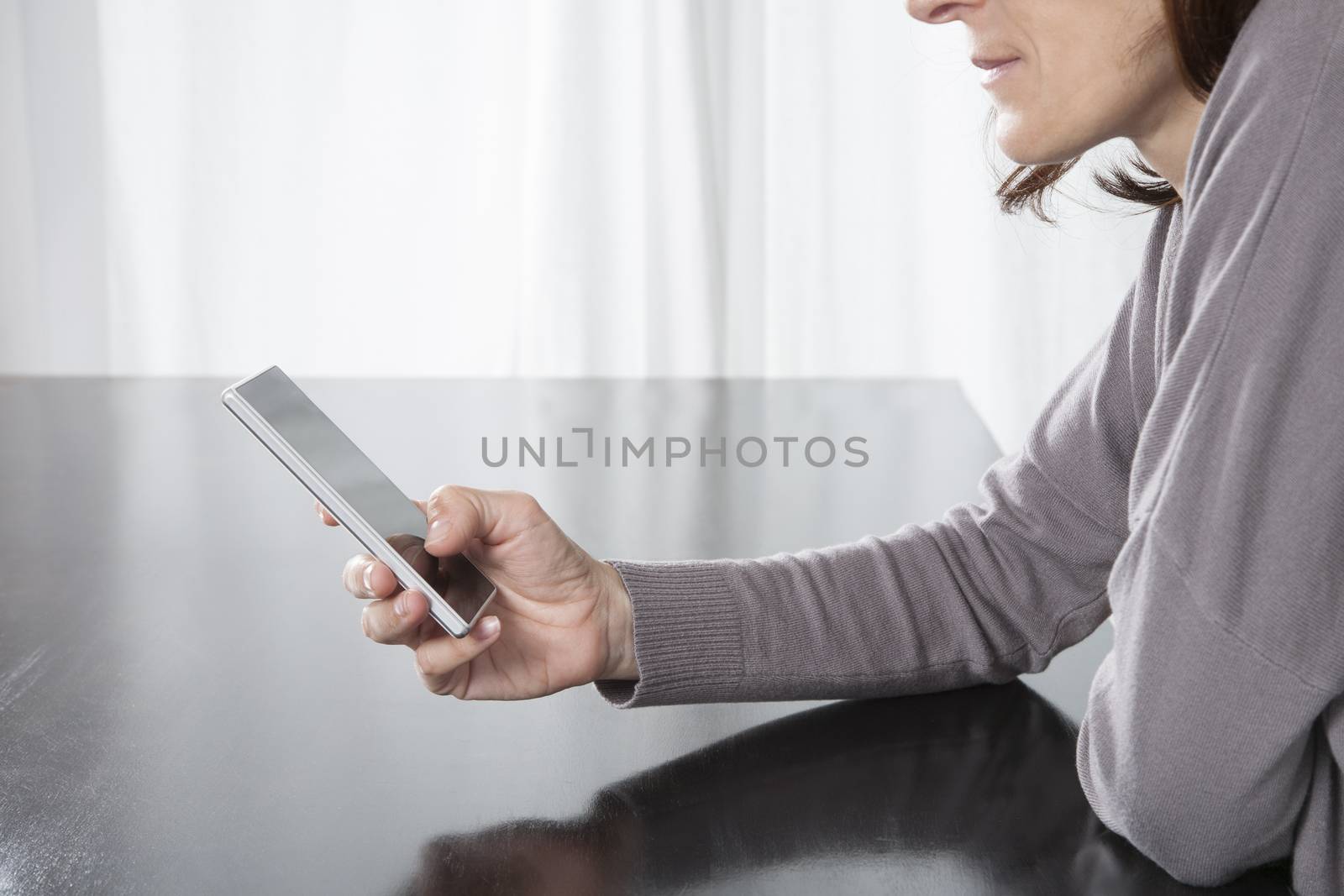 woman hand grey sweater finger touching digital phone mobile blank screen on black reflect table white curtain indoor