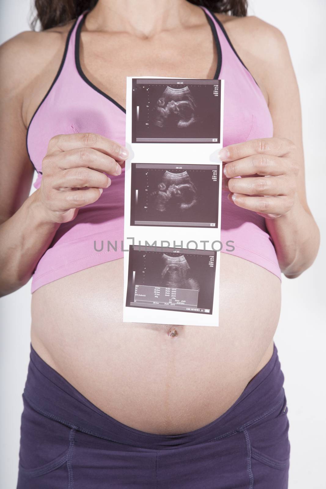 eight months pregnant woman bare belly pink shirt purple trousers with ultrasound baby scan in her hand isolated on white