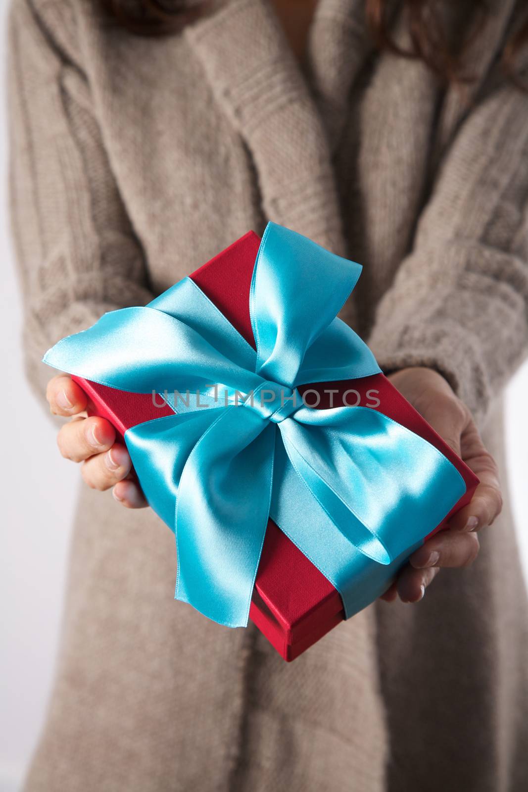 detail of woman brown rustic jacket with a red and blue gift box in her hands offering
