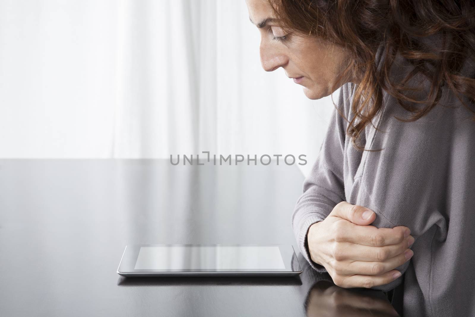 brunette woman grey sweater reading digital tablet blank screen on black reflect table white curtain indoor