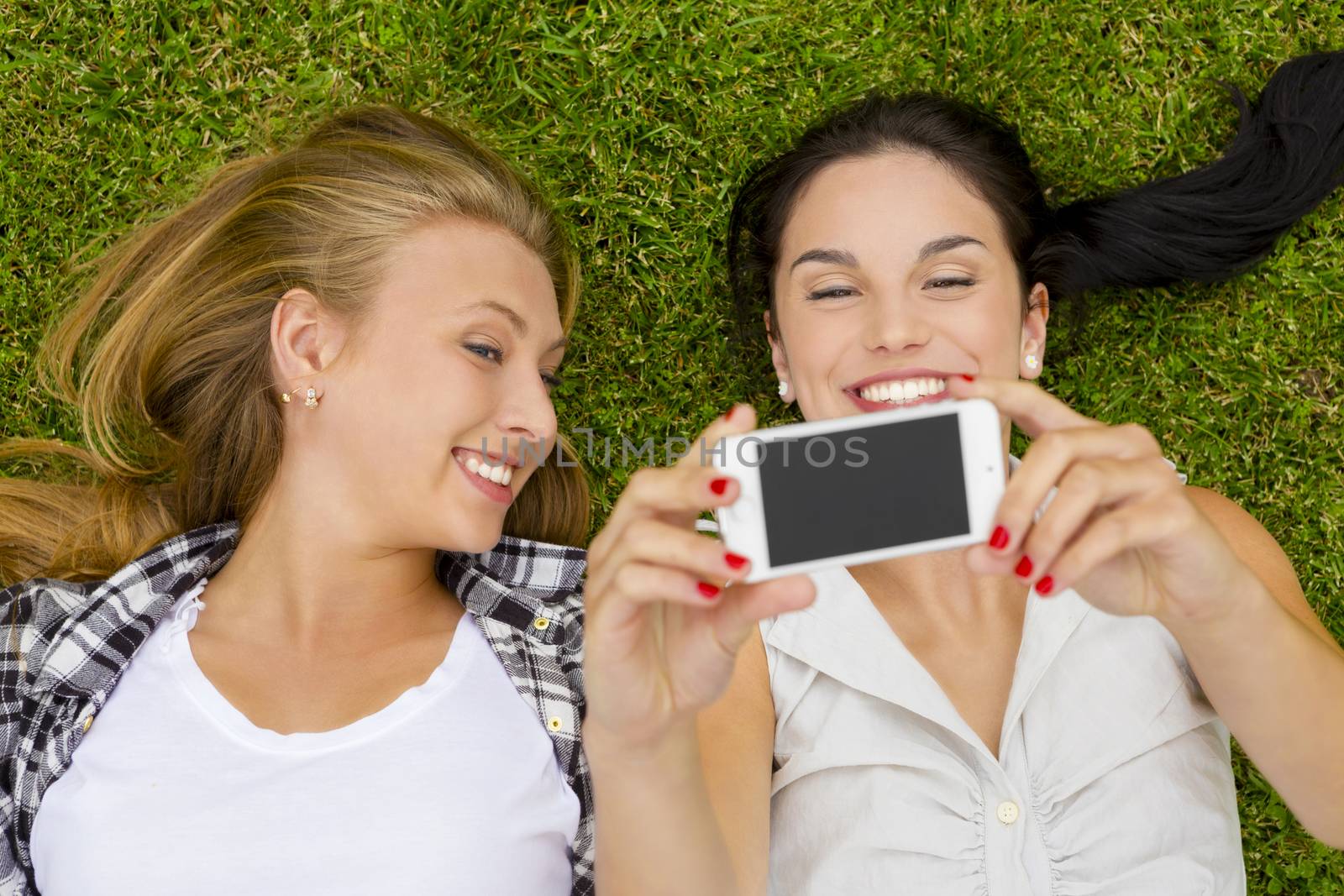 Female best friends lying on the grass and taking selfies