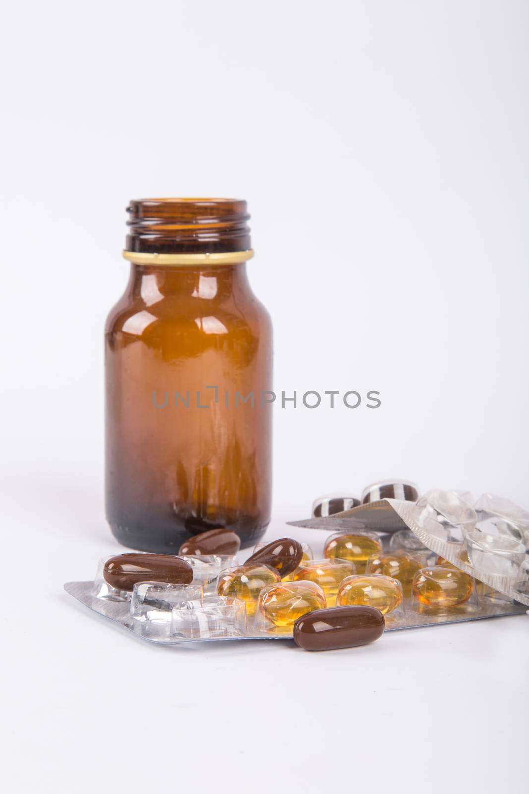 Close-up view of mix of pills and standing brown glass medical bottle, isolated on white background.