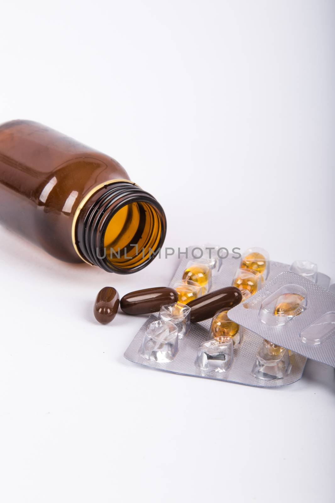 Close-up view of mix of pills and fallen brown glass medical bottle, isolated on white background.