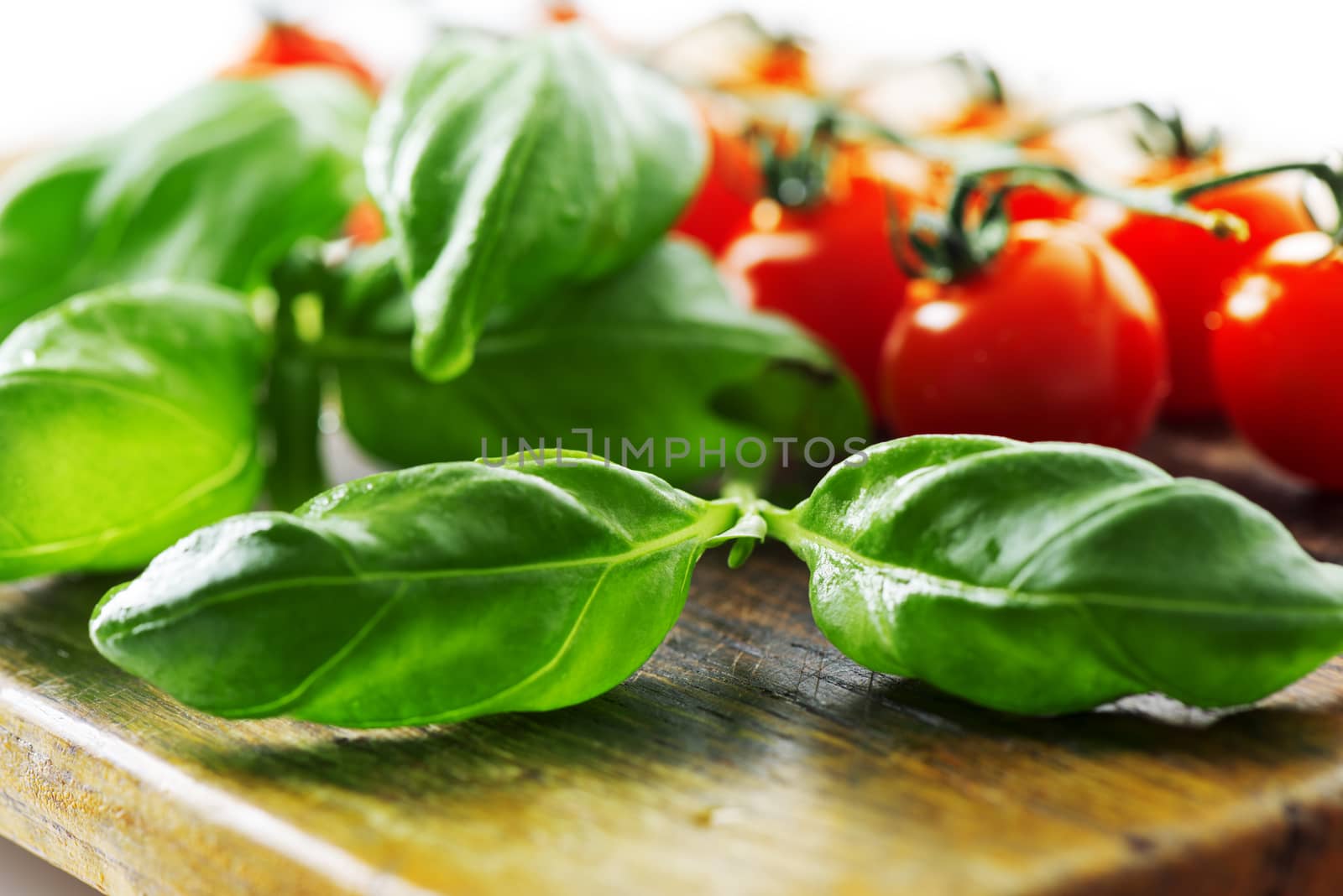 Tomatoes and basil leaf on wooden table close up by Nanisimova