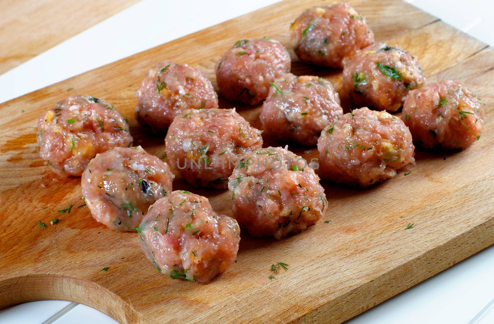 Delicious Raw Meatballs with Greens closeup on Wooden Cutting Board 