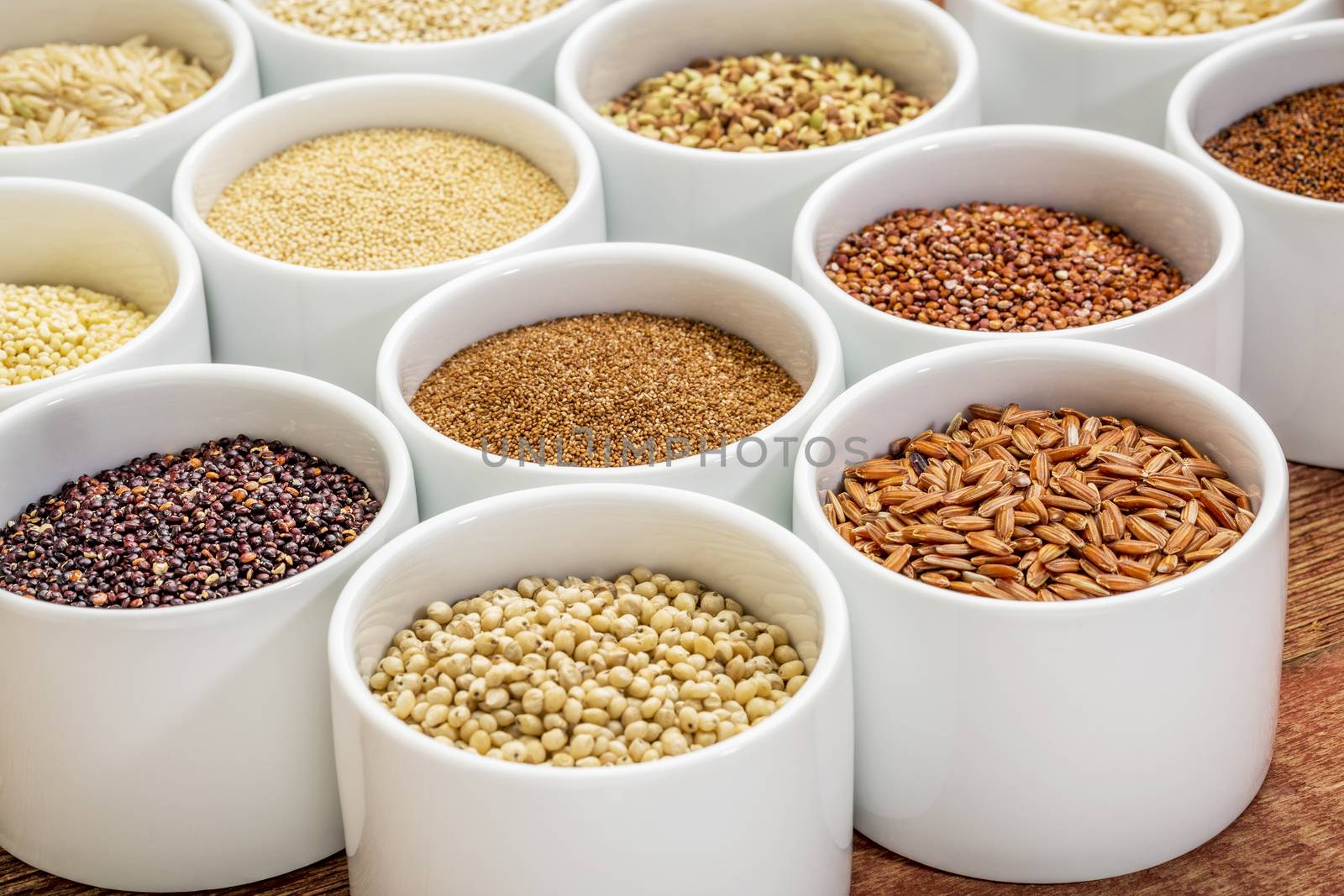 healthy, gluten free grains collection (quinoa, brown rice, millet, amaranth, teff, buckwheat, sorghum), small round bowls against rustic wood