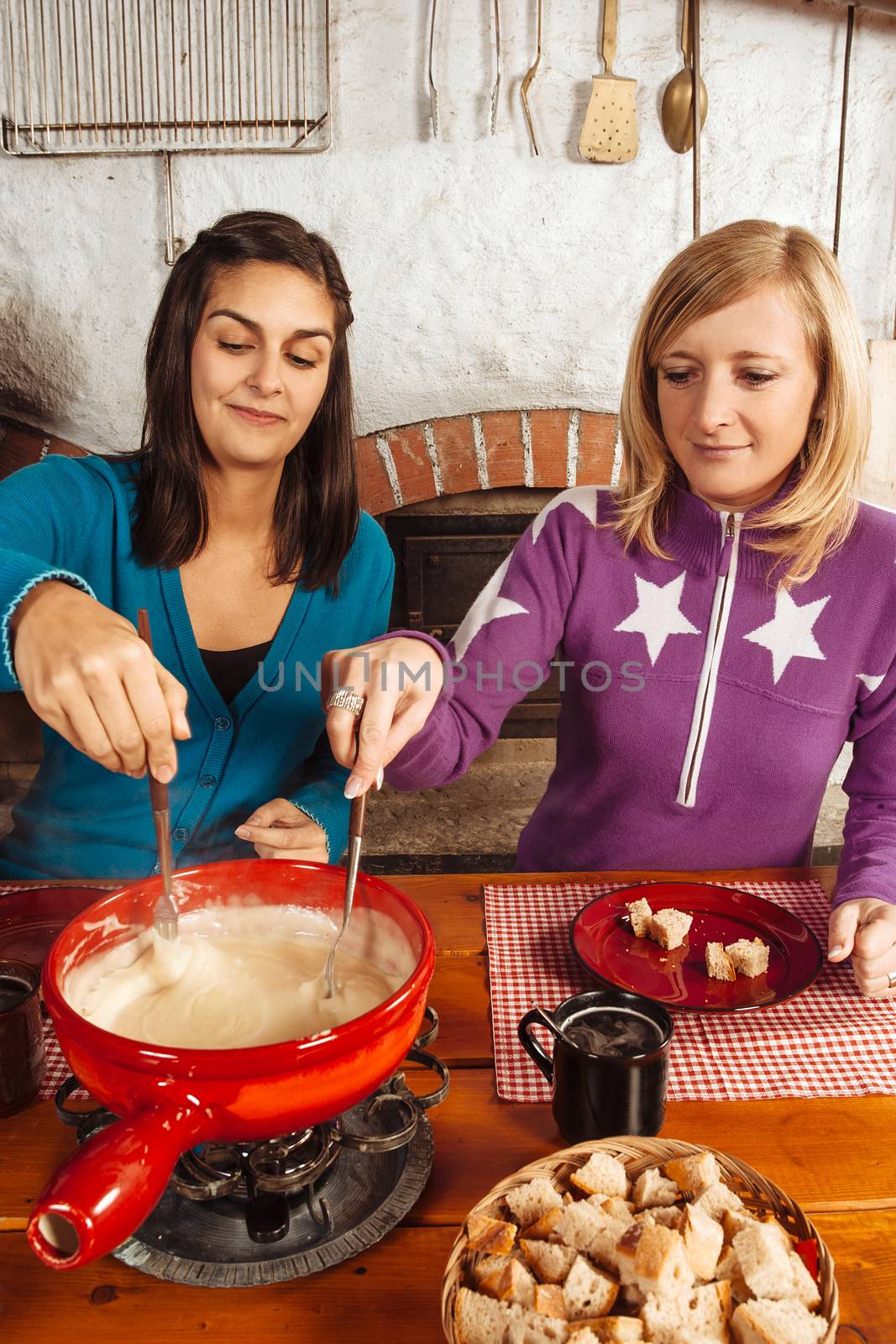 Photo of two beautiful women dipping bread into the melted cheese in a fondue pot.