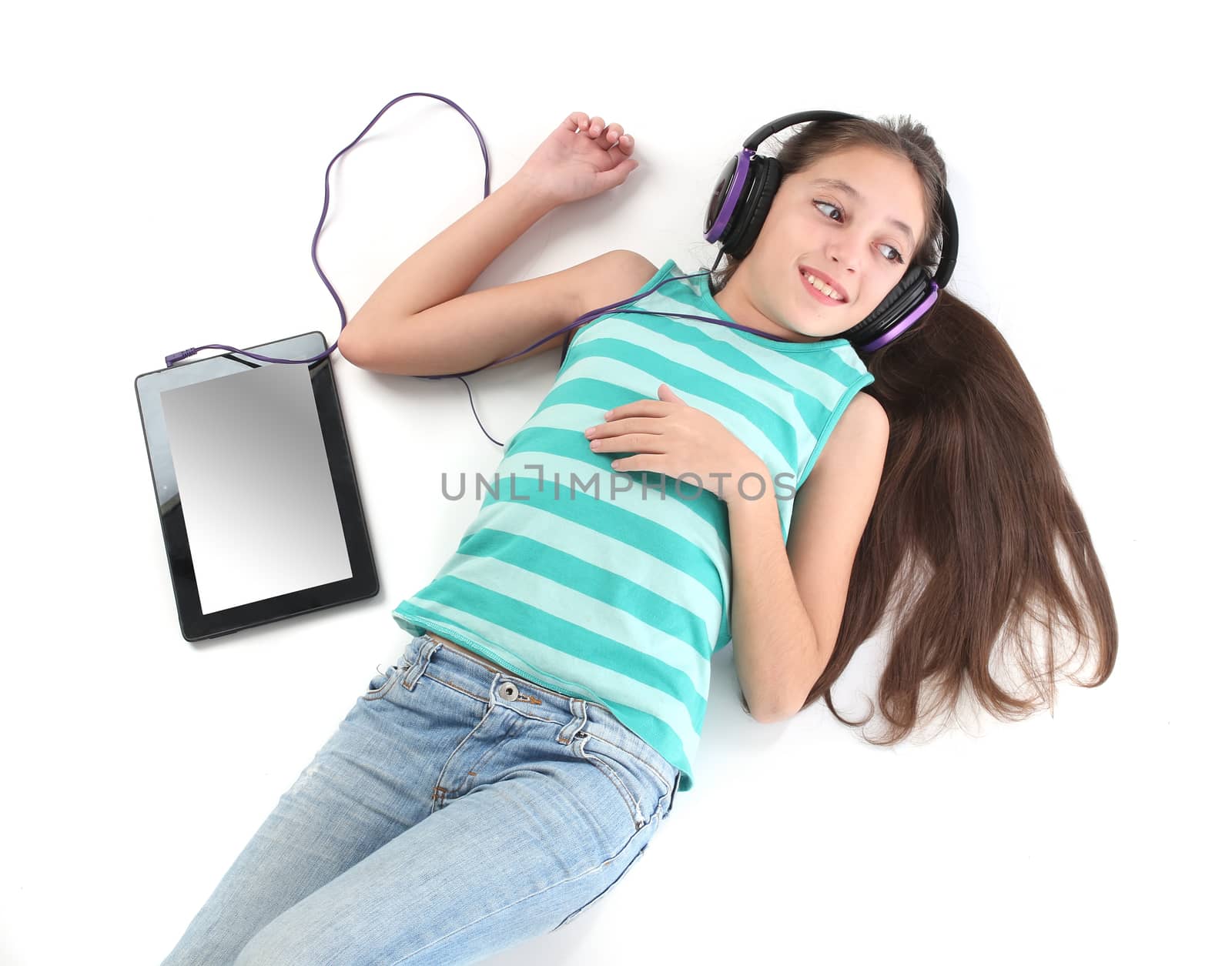 Beautiful pre-teen girl lying on the floor with a tablet computer and headphones. by Erdosain