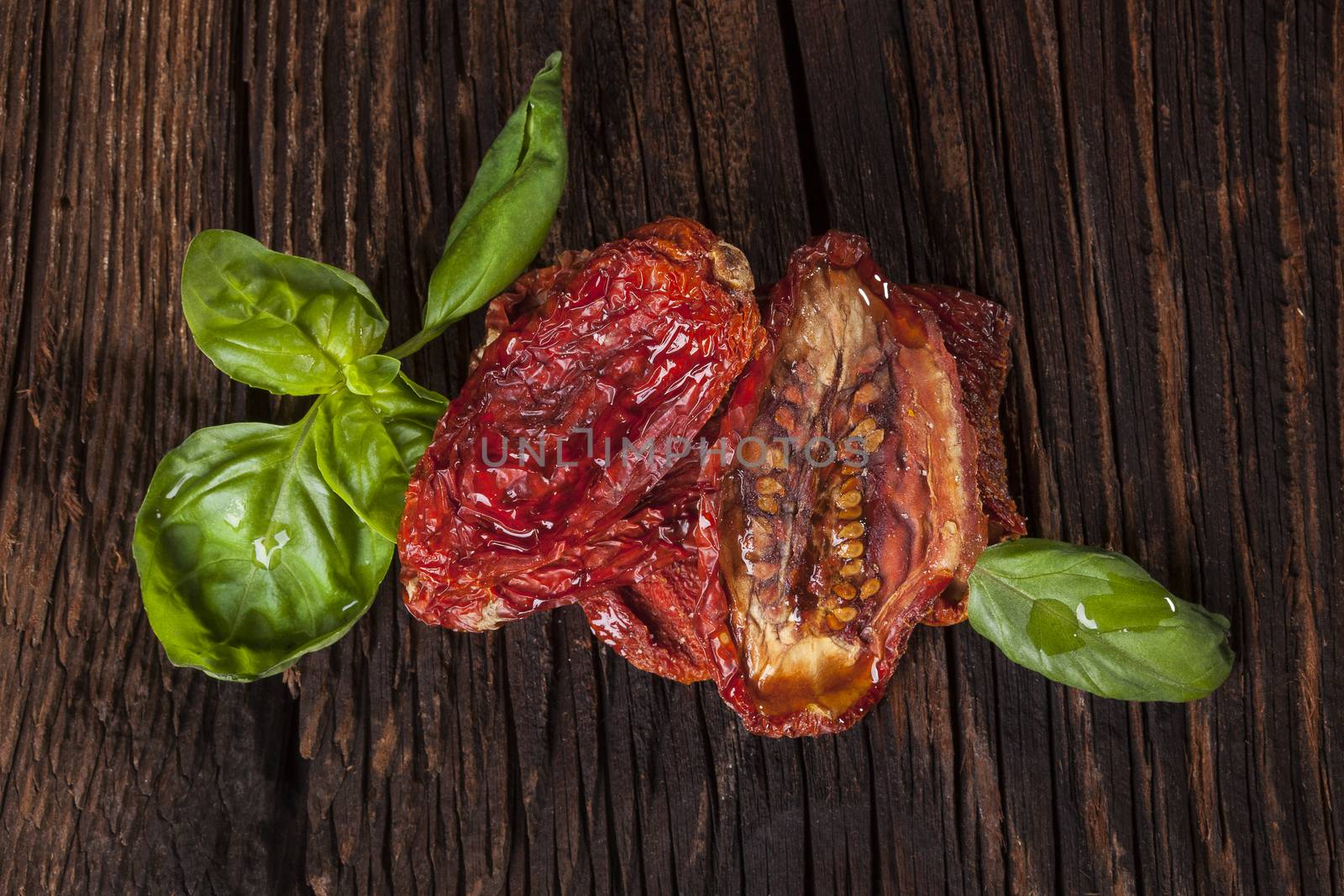 Delicious dried tomatoes and fresh basil on brown wooden vintage textured background. Traditional mediterranean kitchen.