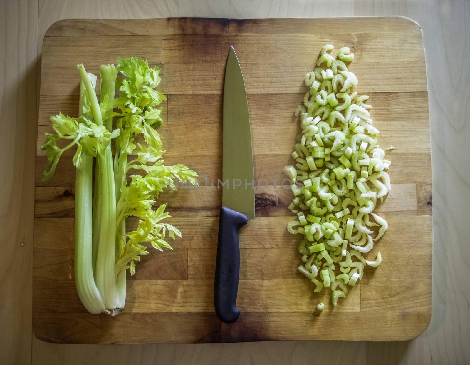 Cutted and whole celery on a wooden board with a knife by weruskak