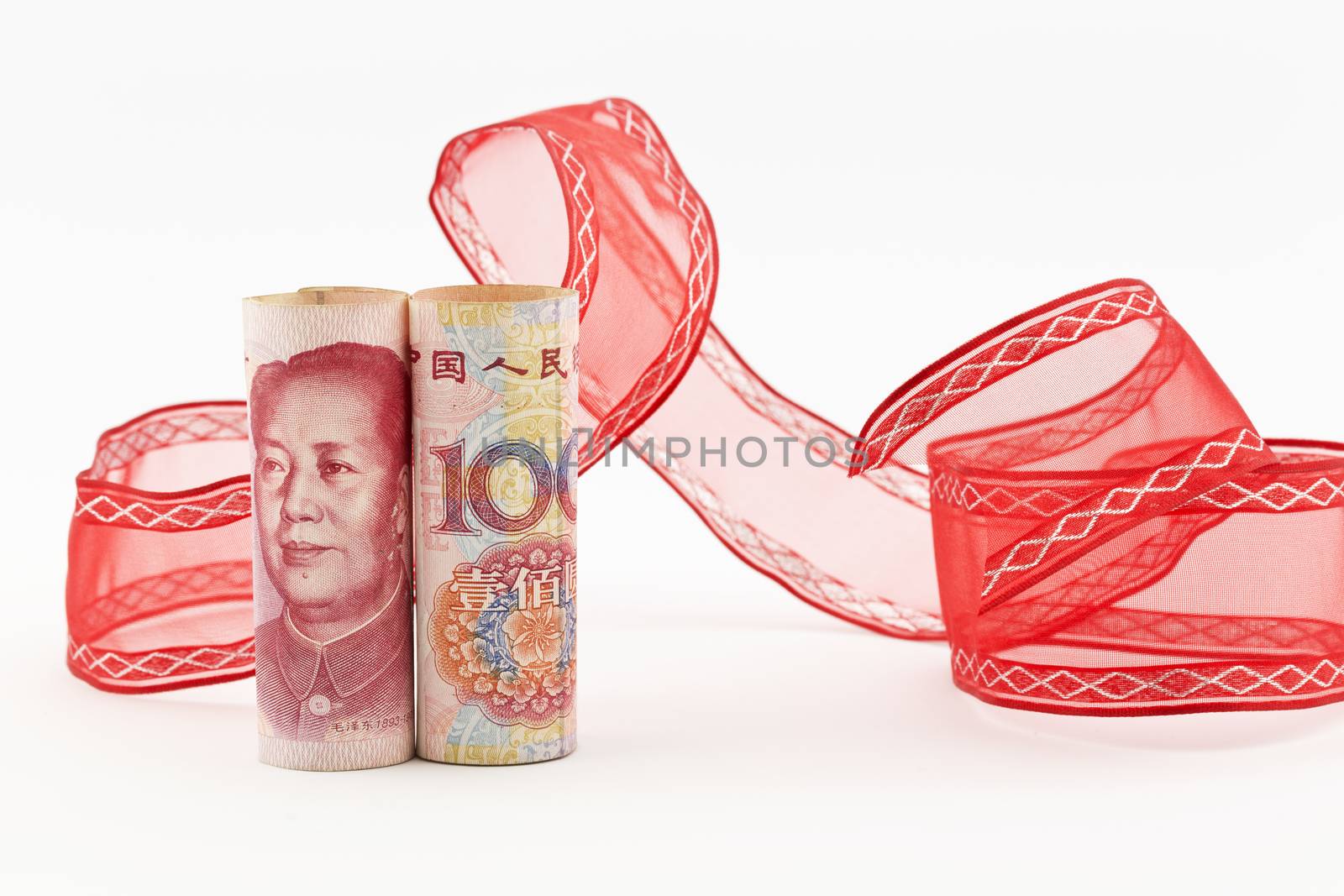 Yuan currency stands upright in front of swirl of red ribbon on white background in horizontal image.  