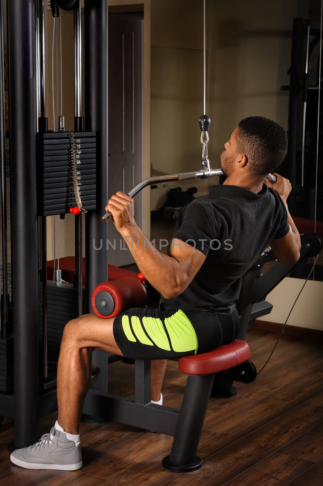 Handsome young african descent mixed race man doing lats pull-down workout in gym