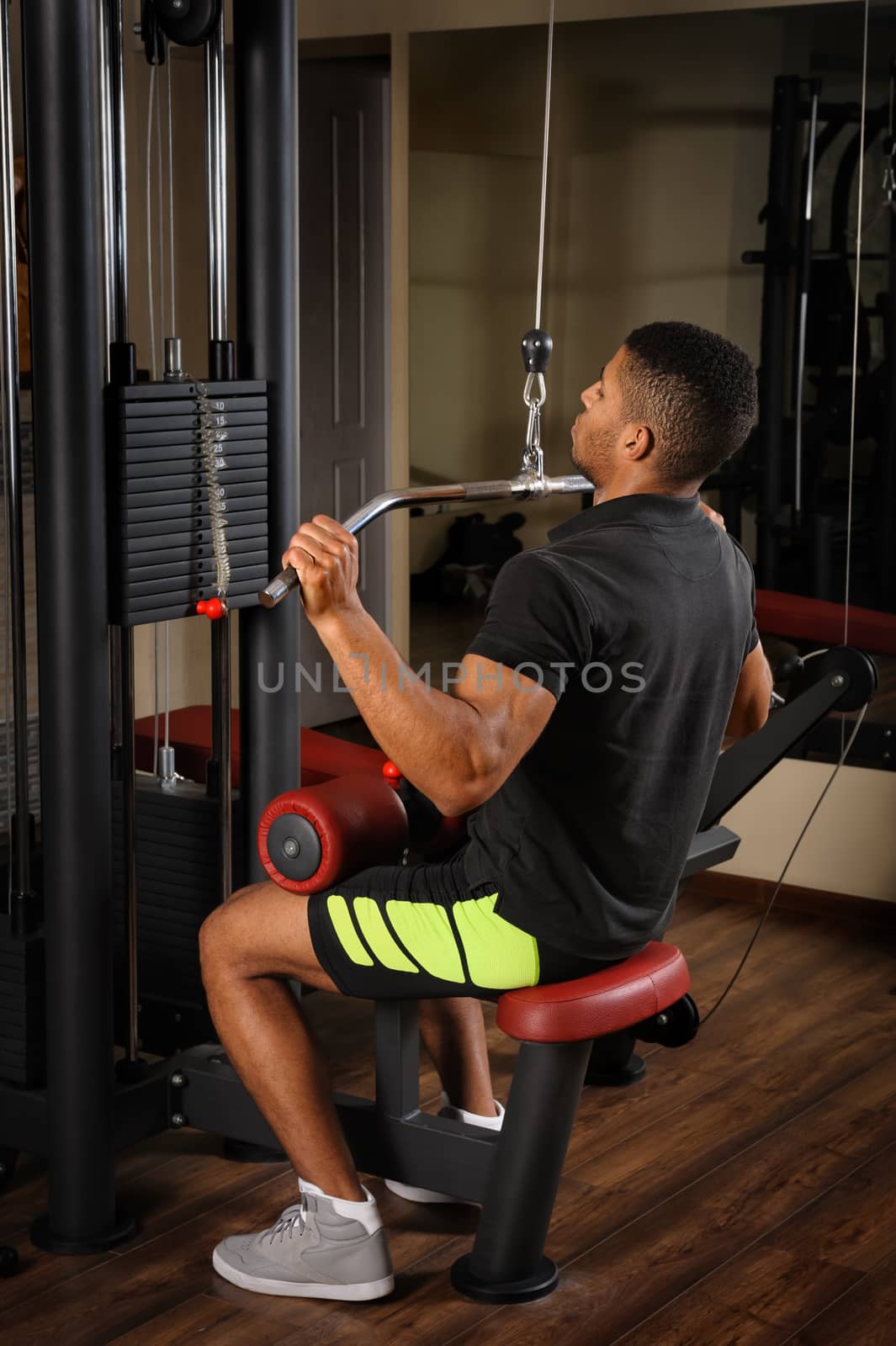 Handsome young african descent mixed race man doing lats pull-down workout in gym