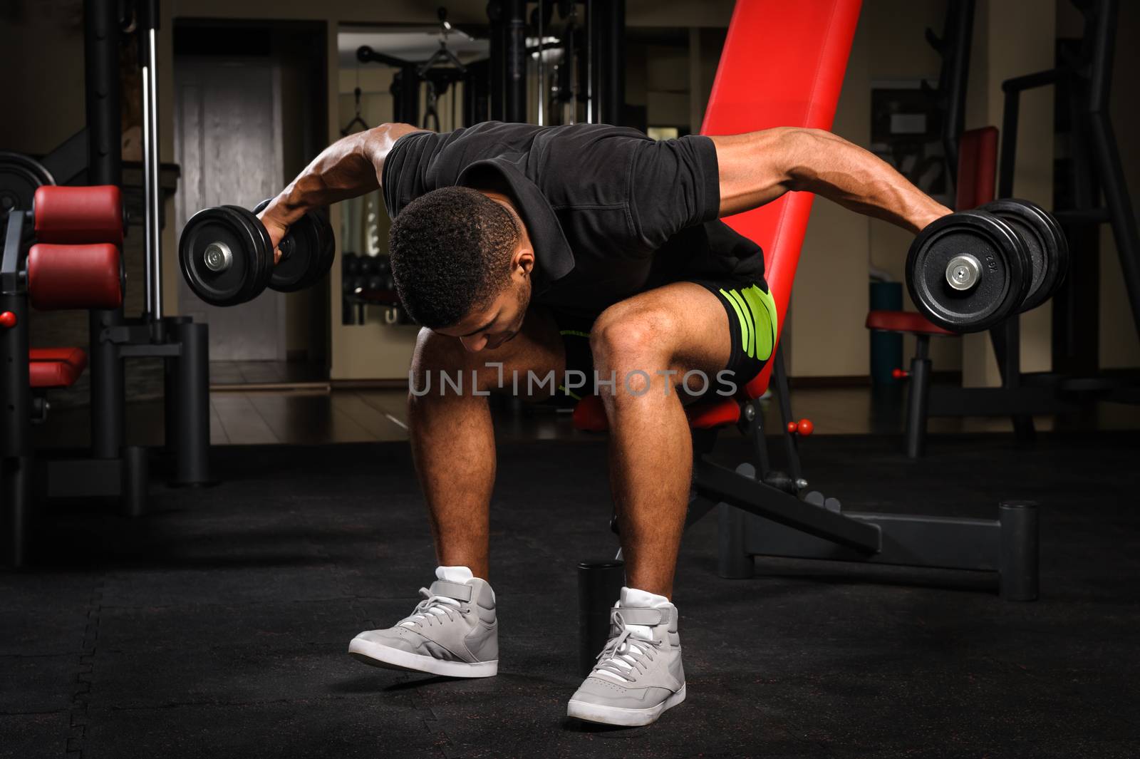 Young man doing Seated Bent Over Dumbbell Reverse Fly workout in gym by starush