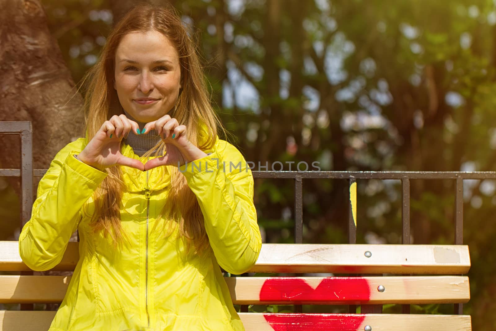 Girl folded her fingers in the form of heart. On a bench in the park