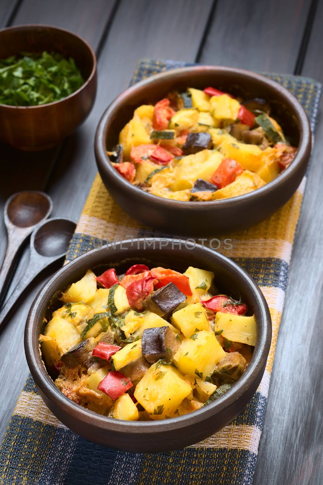 Baked potato, eggplant, zucchini and tomato casserole in rustic bowls, photographed on dark wood with natural light (Selective Focus, Focus in the middle of the first dish)