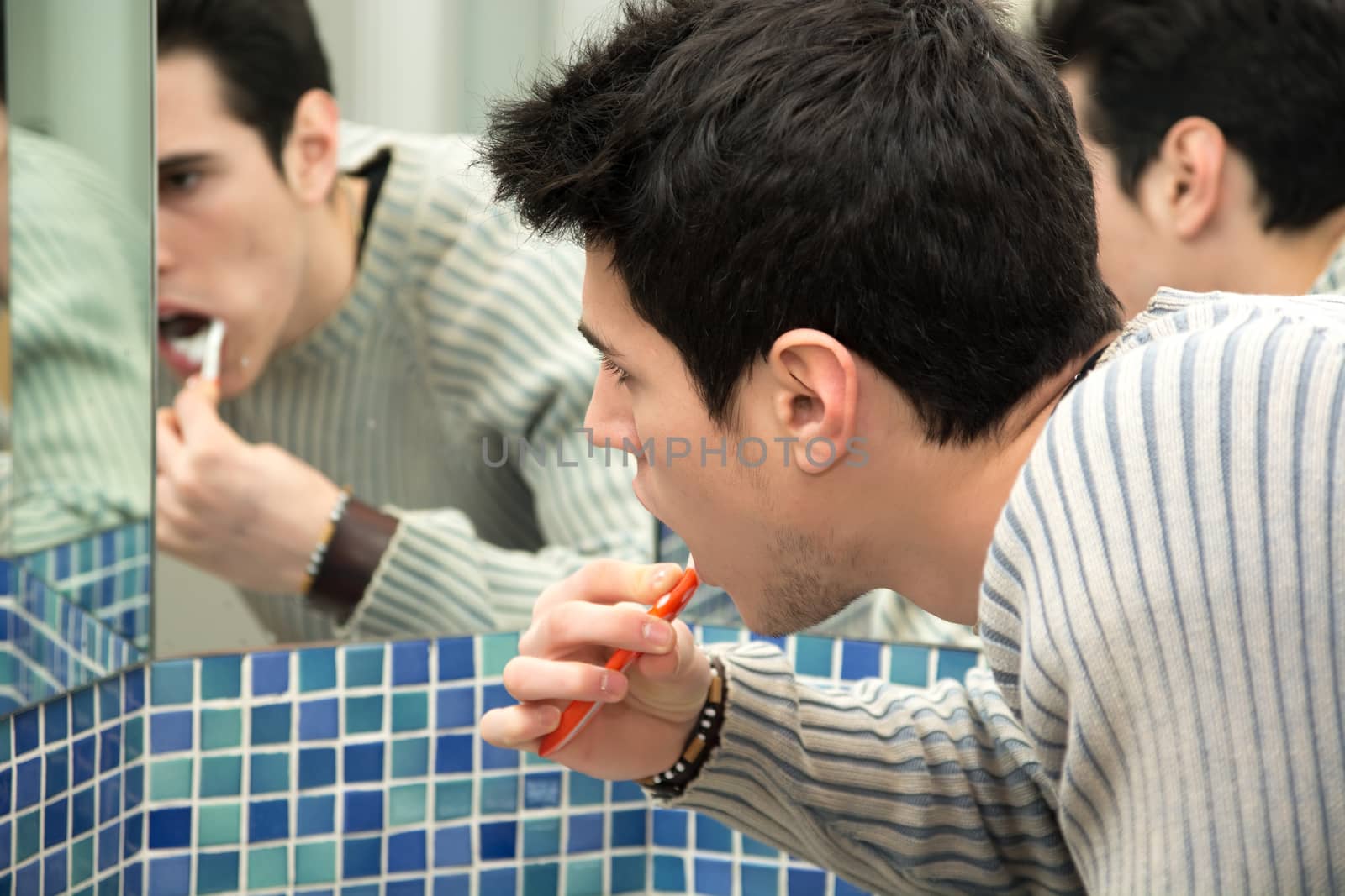 Headshot of attractive young man brushing teeth with toothbrush, looking at himself in mirror Headshot of attractive young man brushing teeth with toothbrush, looking at himself in mirror