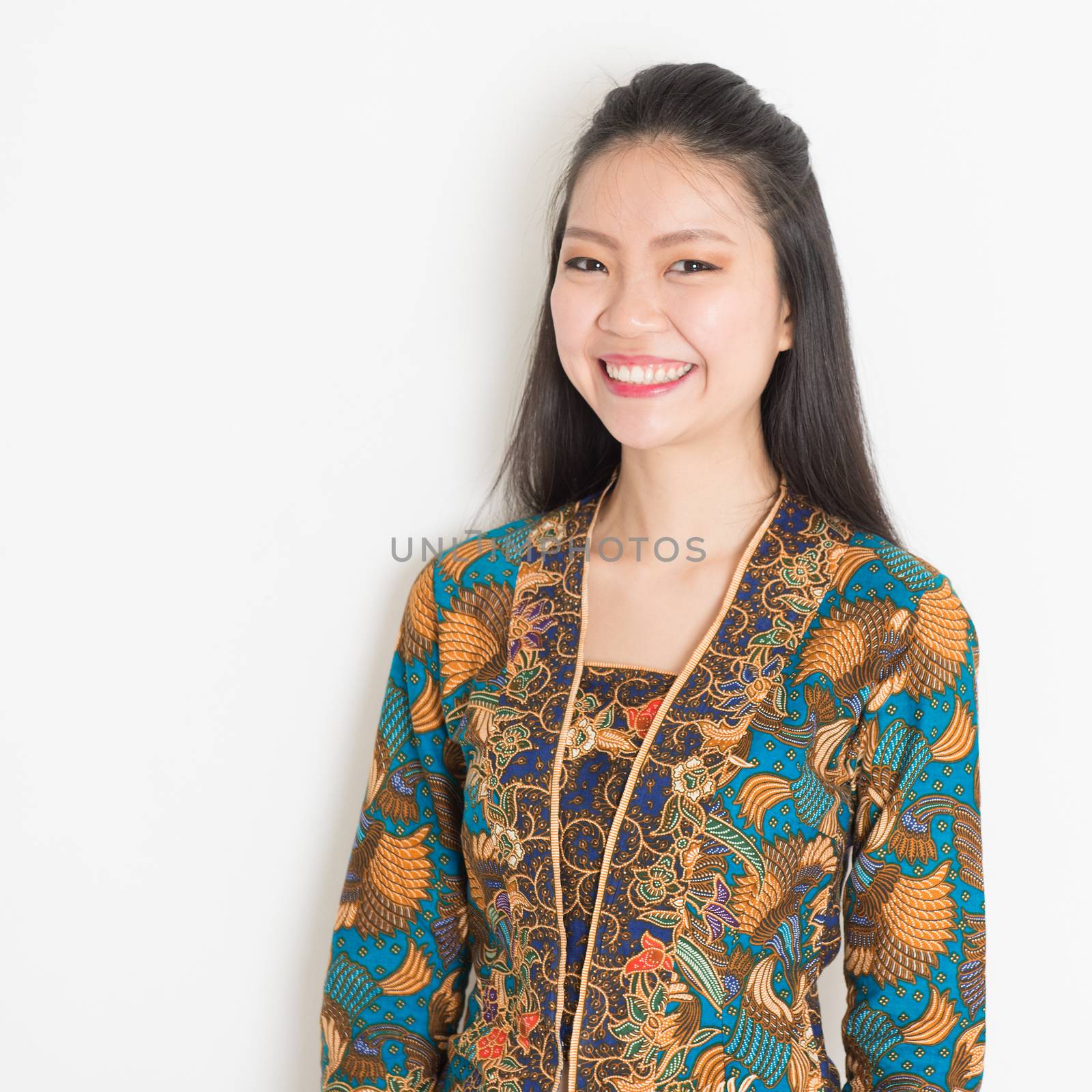 Portrait of Southeast Asian woman in batik dress on plain background.
