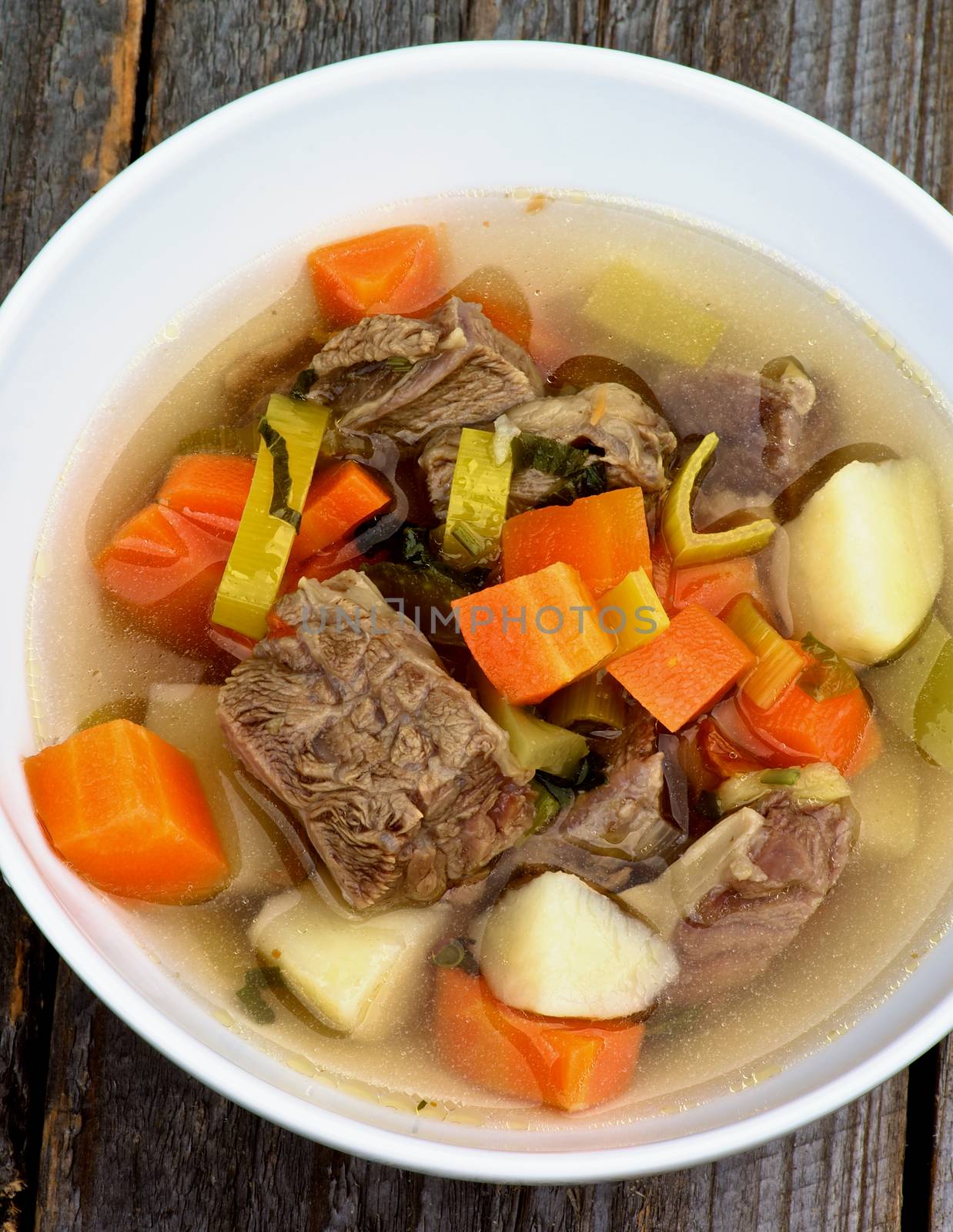 Homemade Beef Soup with Potato, Carrot and Leek in White Bowl Cross Secyion on Wooden background. Top View