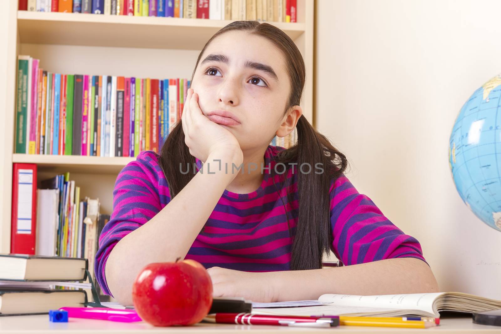 Schoolgirl overwhelmed by her studies, sitting in a table full of notebooks and pencils and pens