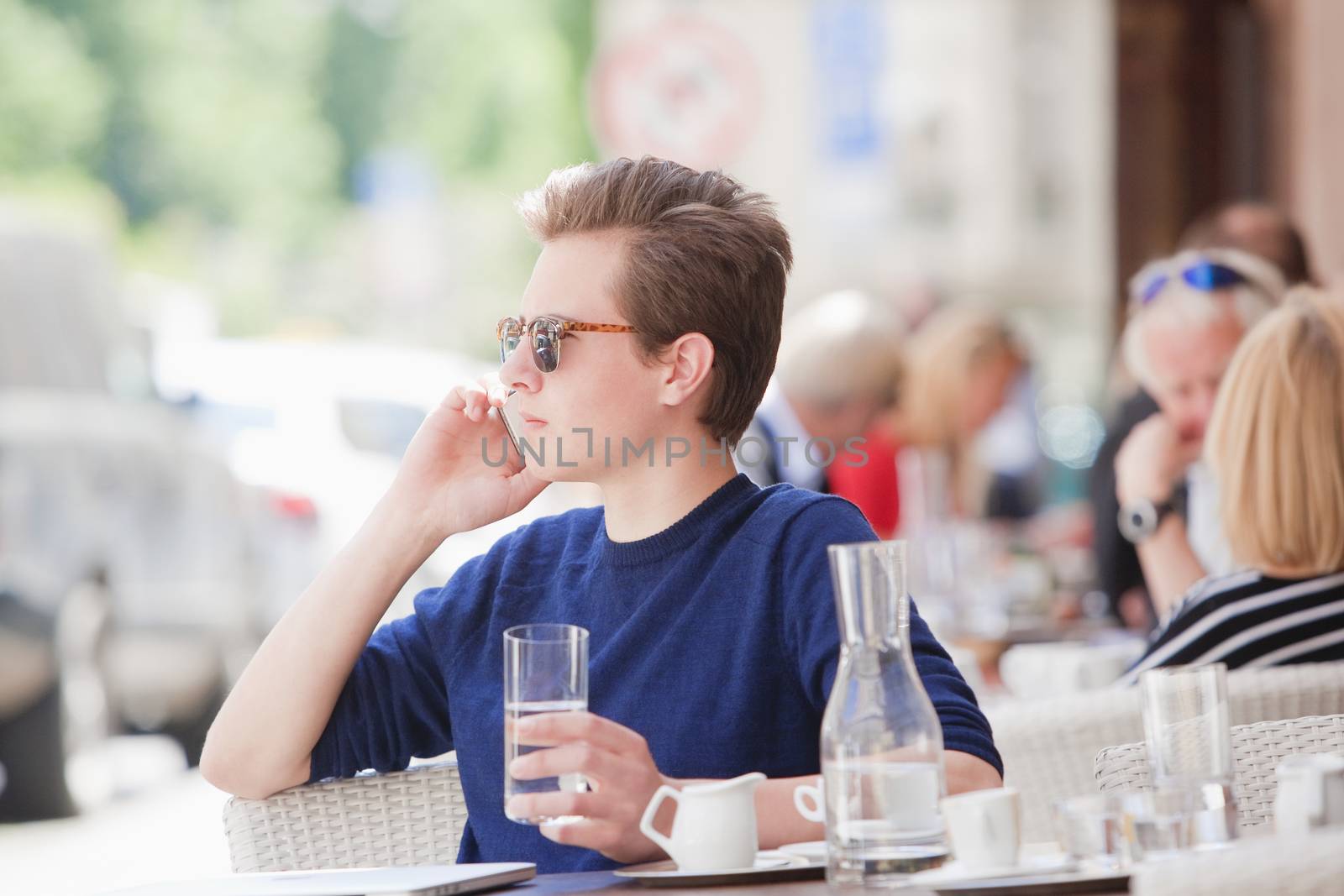 Young Man Sitting in Outside Coffeehouse Talking on Cell Phone