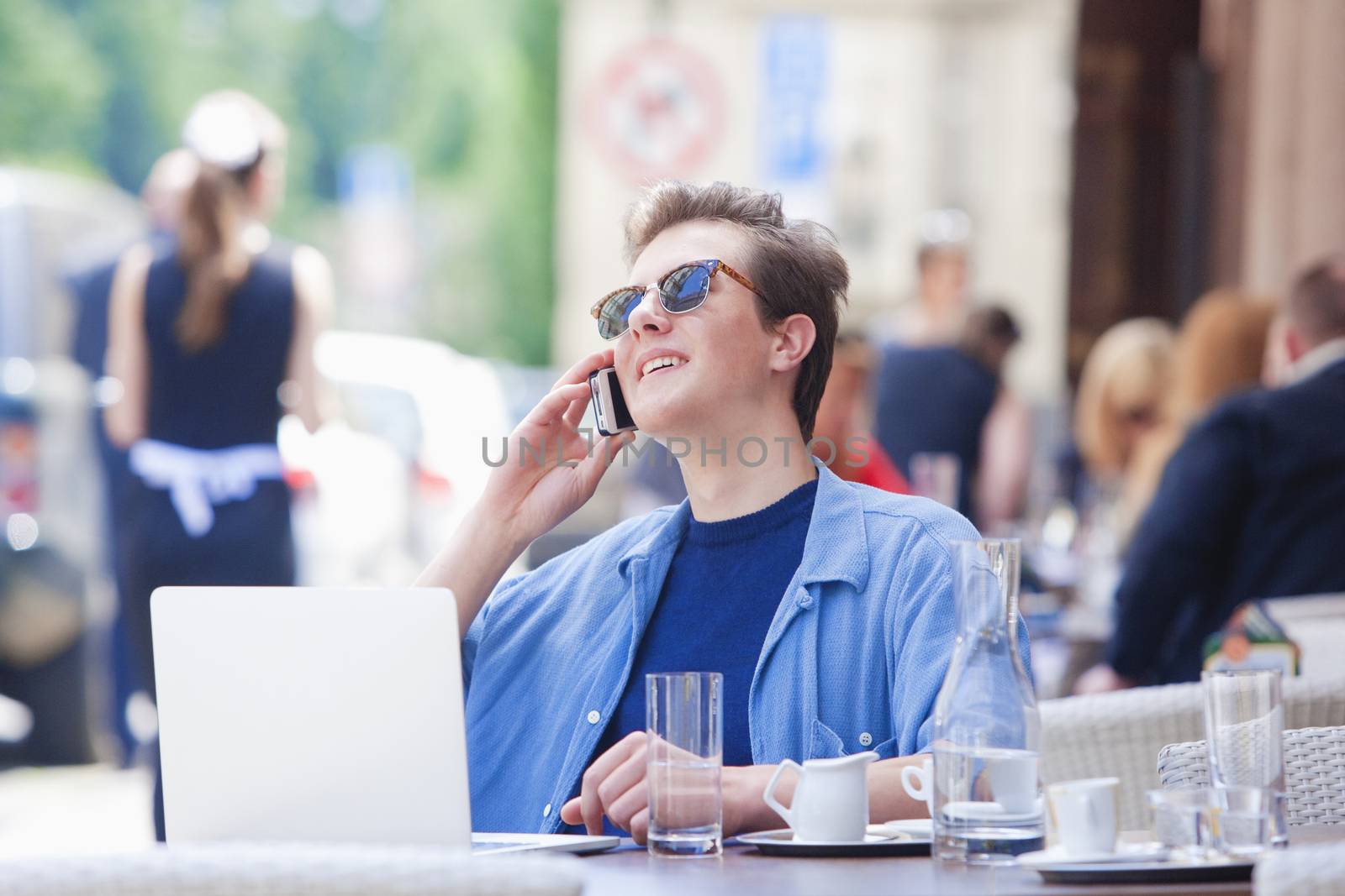 Young Man Sitting in Outside Coffeehouse Talking on Phone by courtyardpix