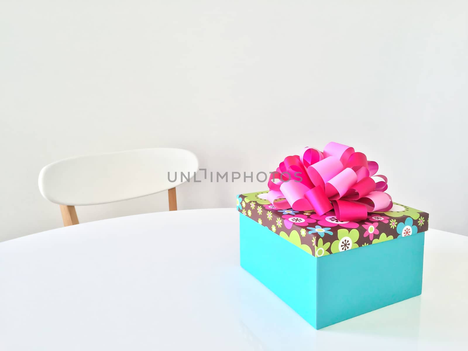 Bright gift box with pink ribbon, on white table.