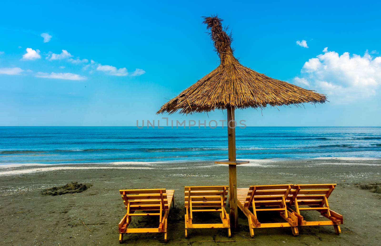 Seaside beach with lounge chairs and straw umbrella.