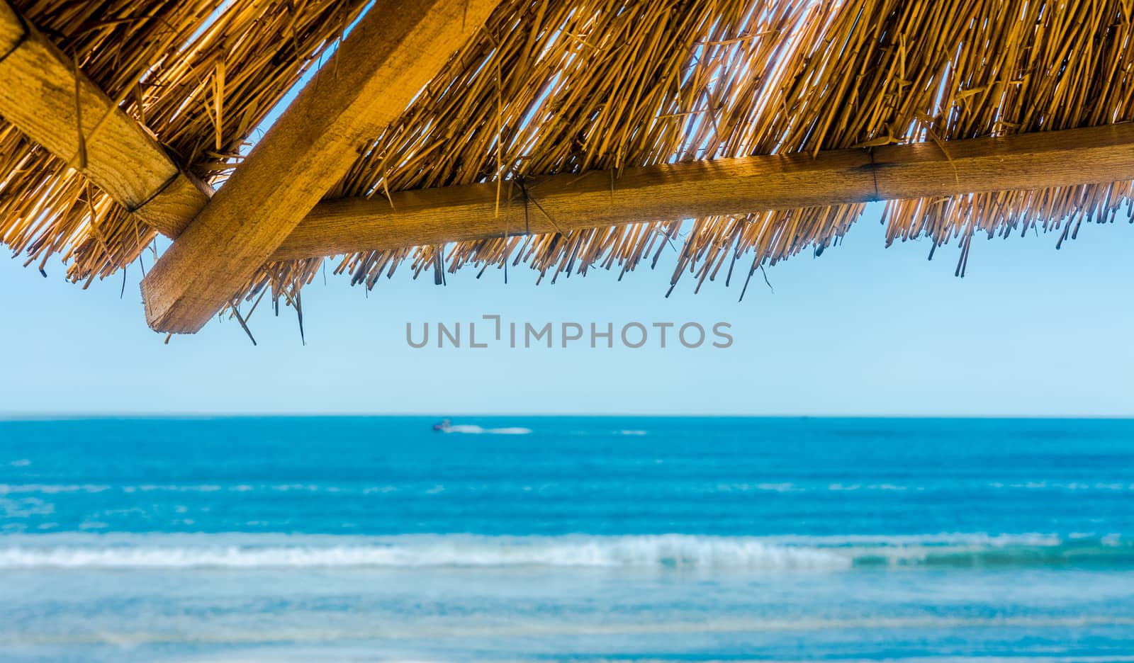 Sea skyline from under straw sun umbrella.