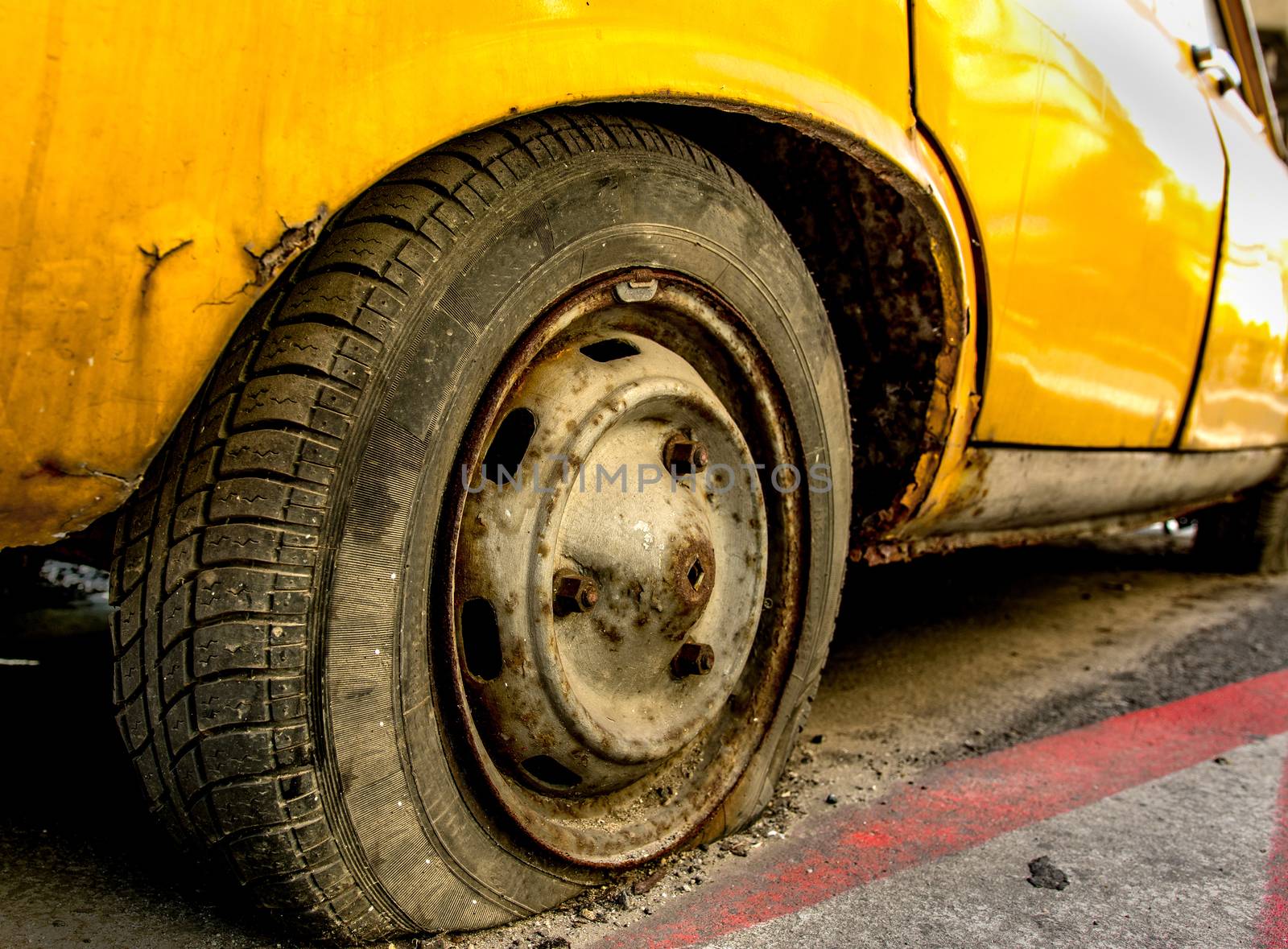 Flat tire of an old yellow car with rusted rim.