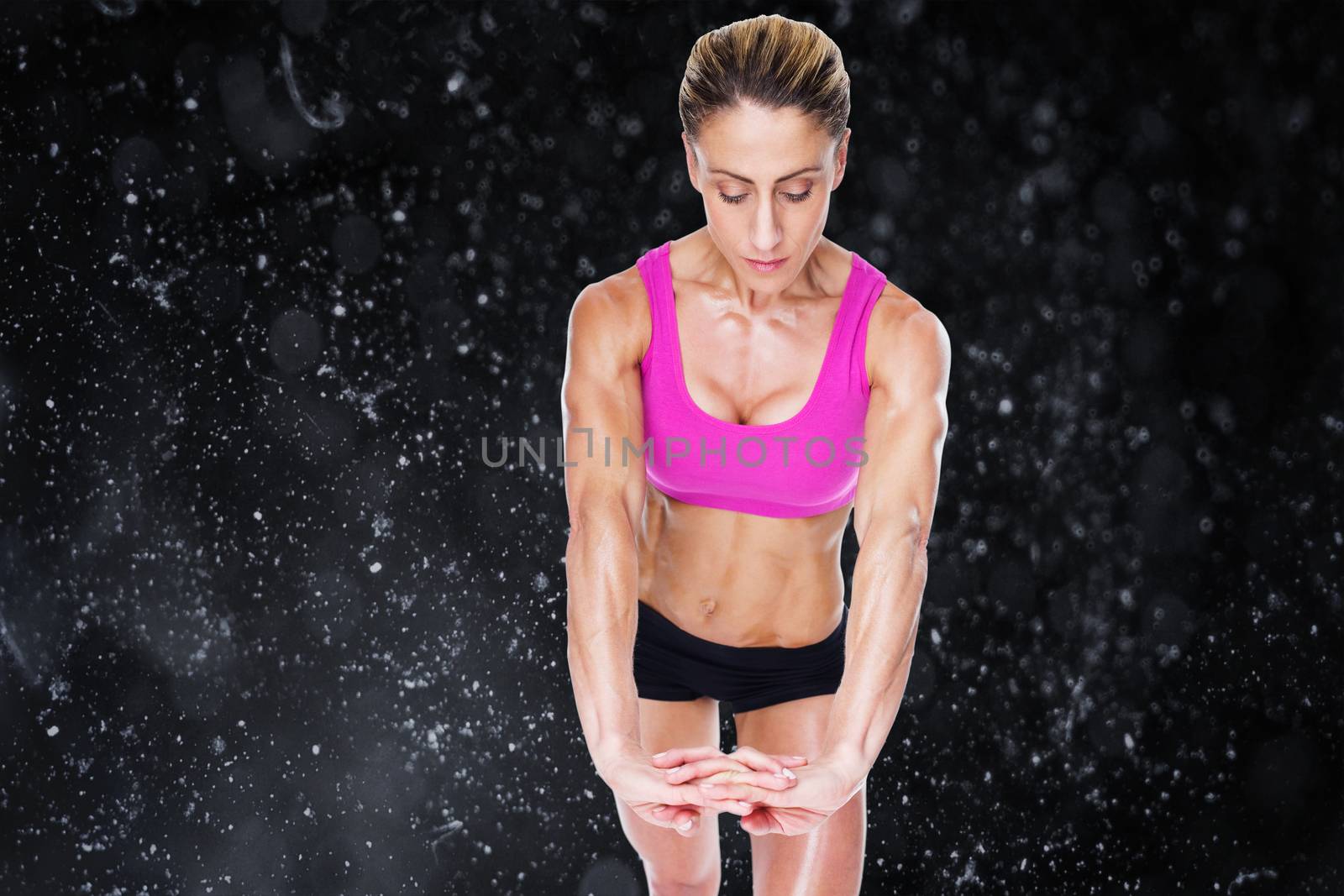 Female bodybuilder flexing with hands together against black background