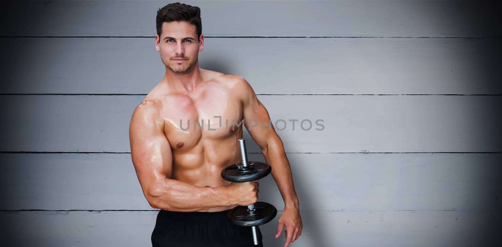 Bodybuilder lifting dumbbell against painted blue wooden planks