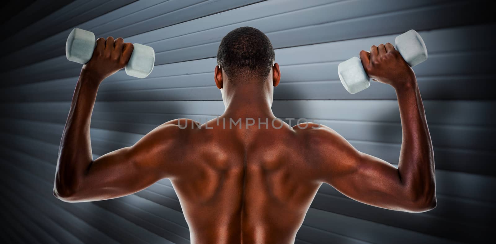 Rear view of a fit shirtless man lifting dumbbells against grey shutters