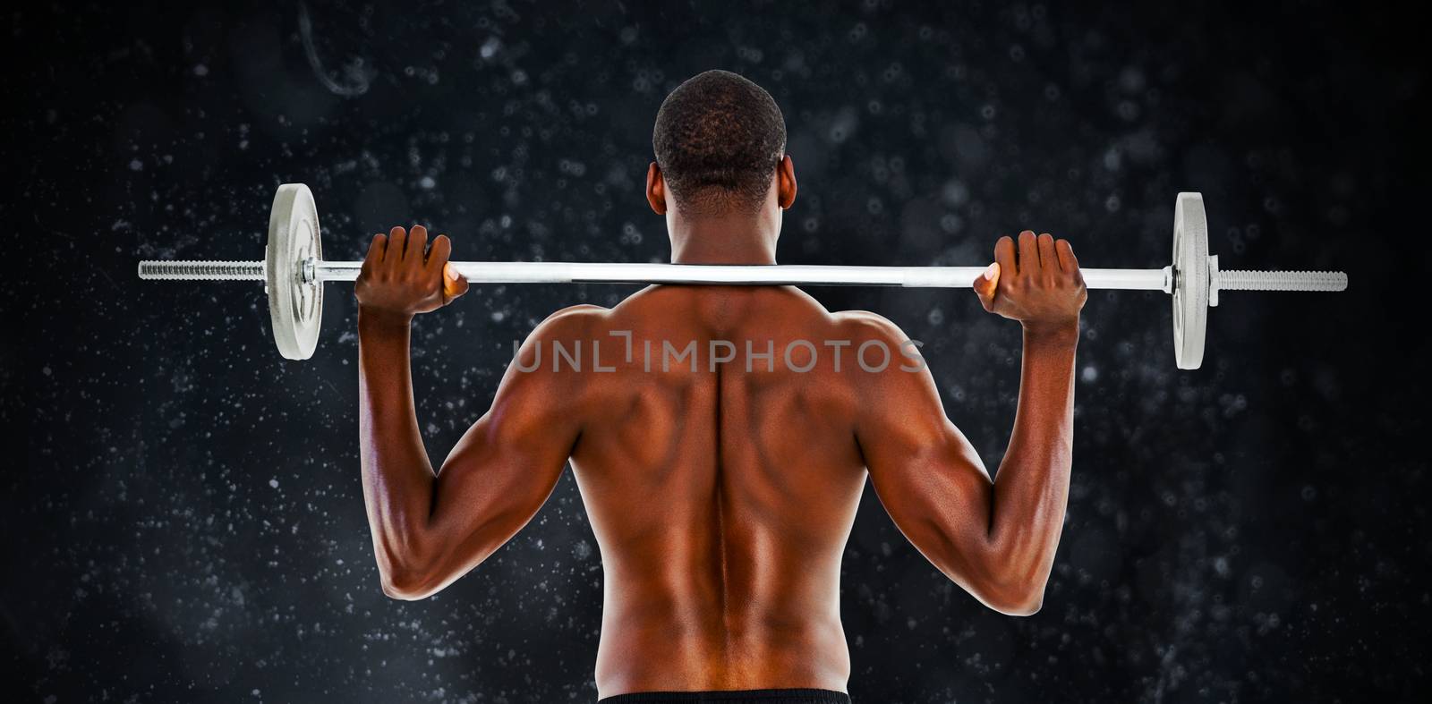 Rear view of a fit shirtless man lifting barbell against black background