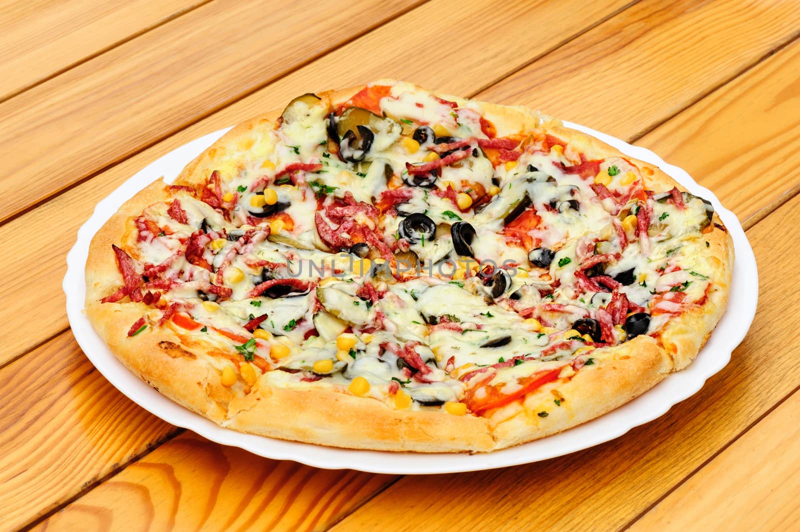 Whole pizza with cut pepperoni, black olives, corn, cheese and pickled cucumbers