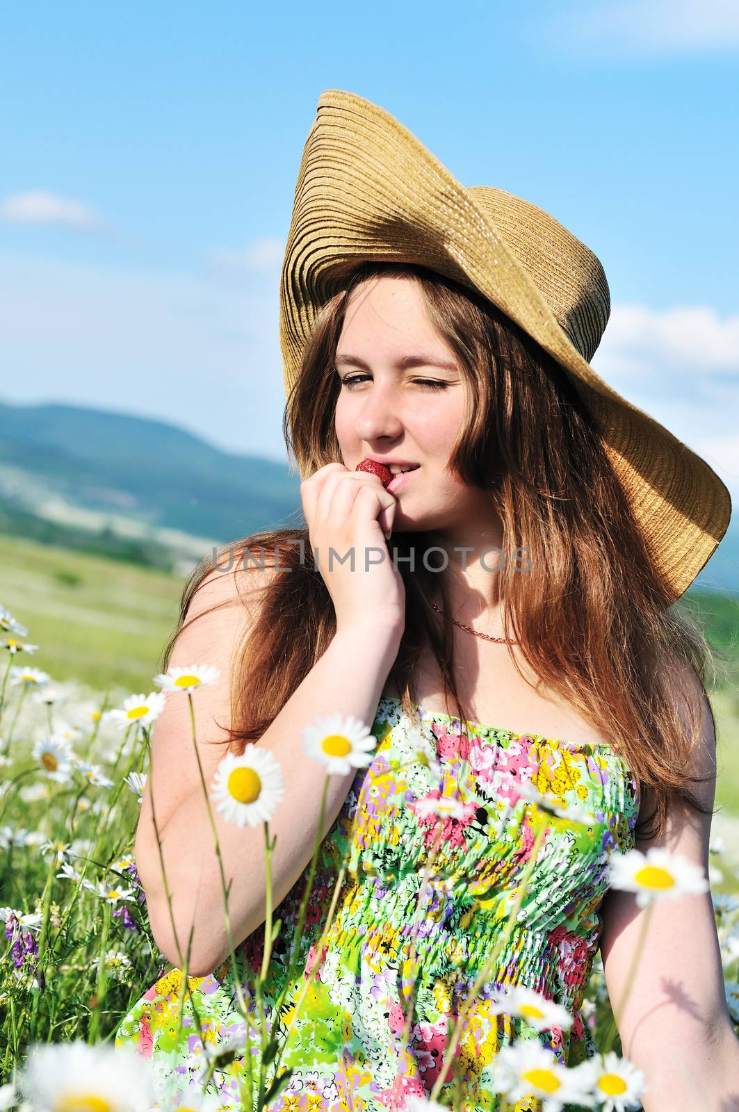 beautiful teen girl wearing srtaw hat enjoying strawberry in daisy field 