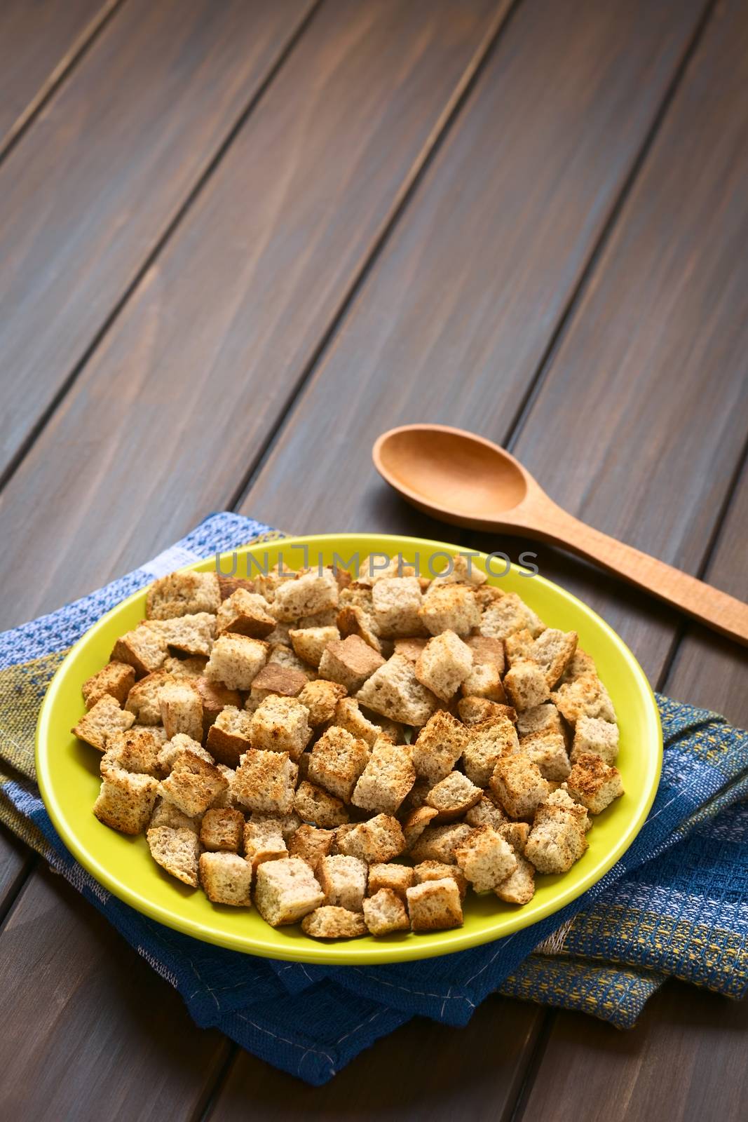 Freshly toasted homemade croutons made of wholegrain bread, photographed on dark wood with natural light (Selective Focus, Focus one third into the croutons)