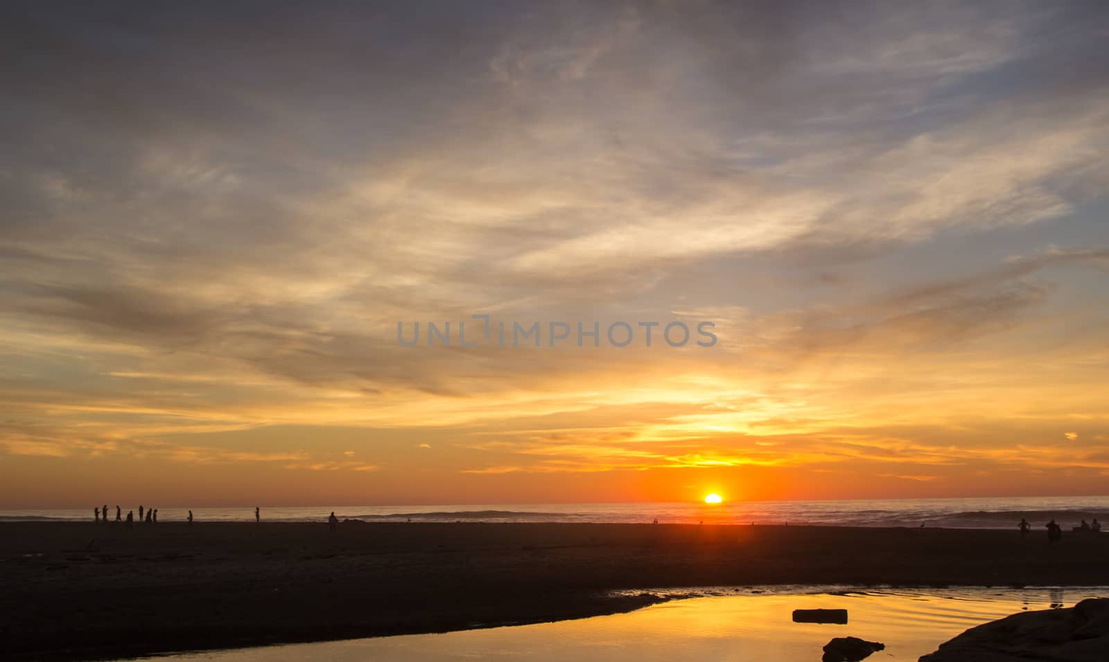 The sun setting over a beach on the west coast as people enjoy the last light of day.